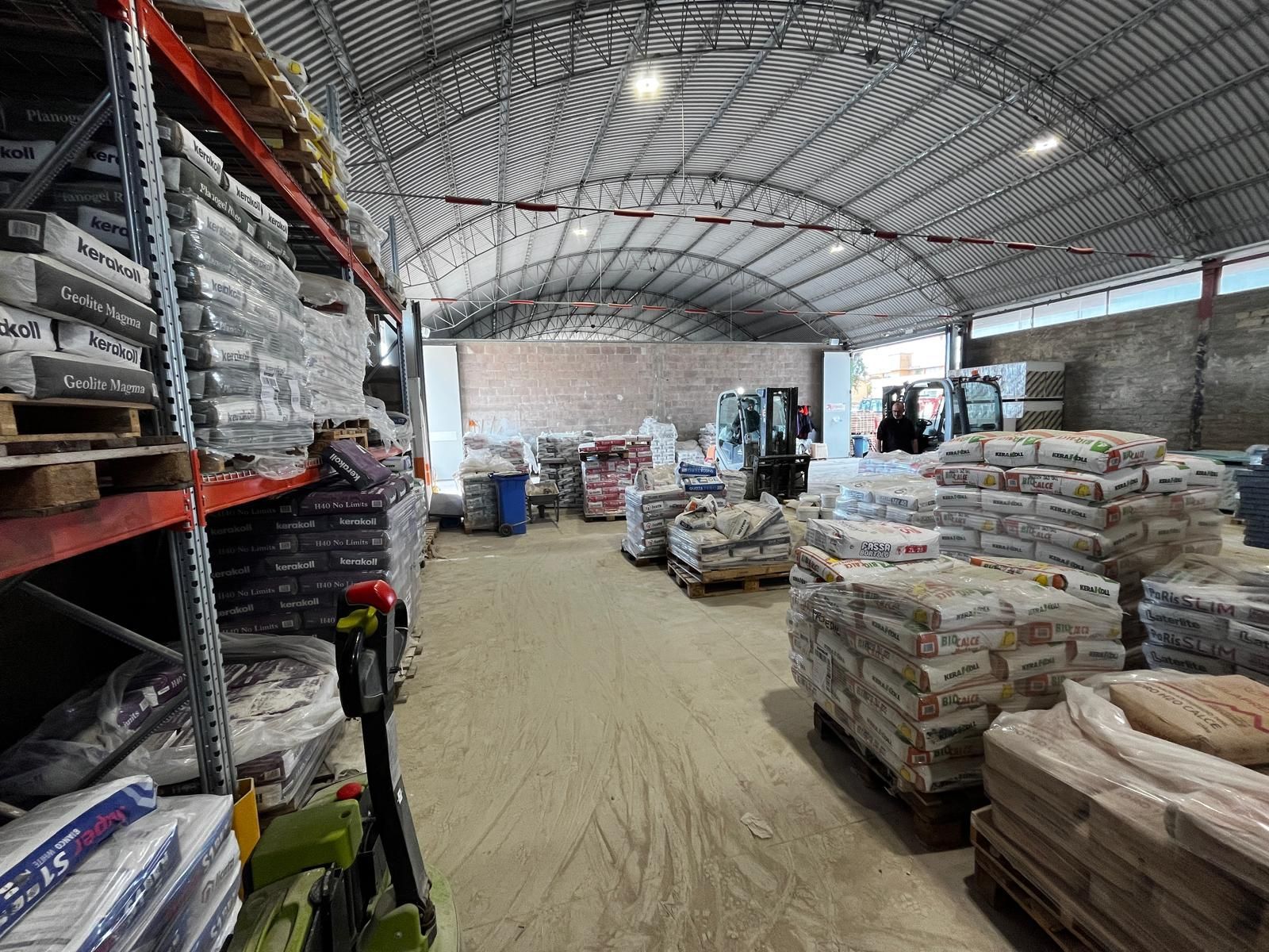Carrello elevatore in un deposito di ghiaia pieno di pile di mattoni e materiali da costruzione sotto un cielo azzurro e limpido.
