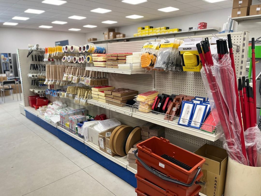 Scaffali pieni di attrezzi e materiali da costruzione all'interno di un negozio ben illuminato.