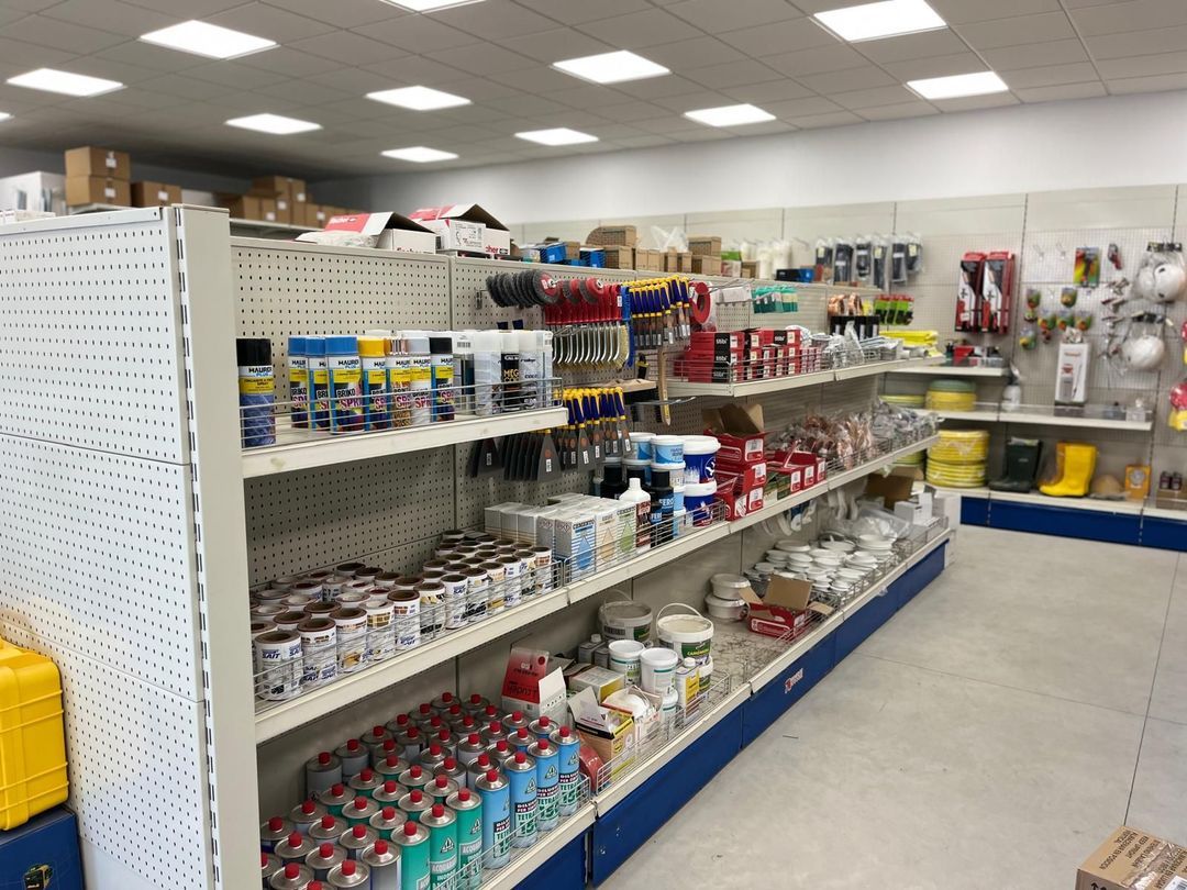 Interno di un negozio di ferramenta con scaffali pieni di vari utensili, vernici e forniture.