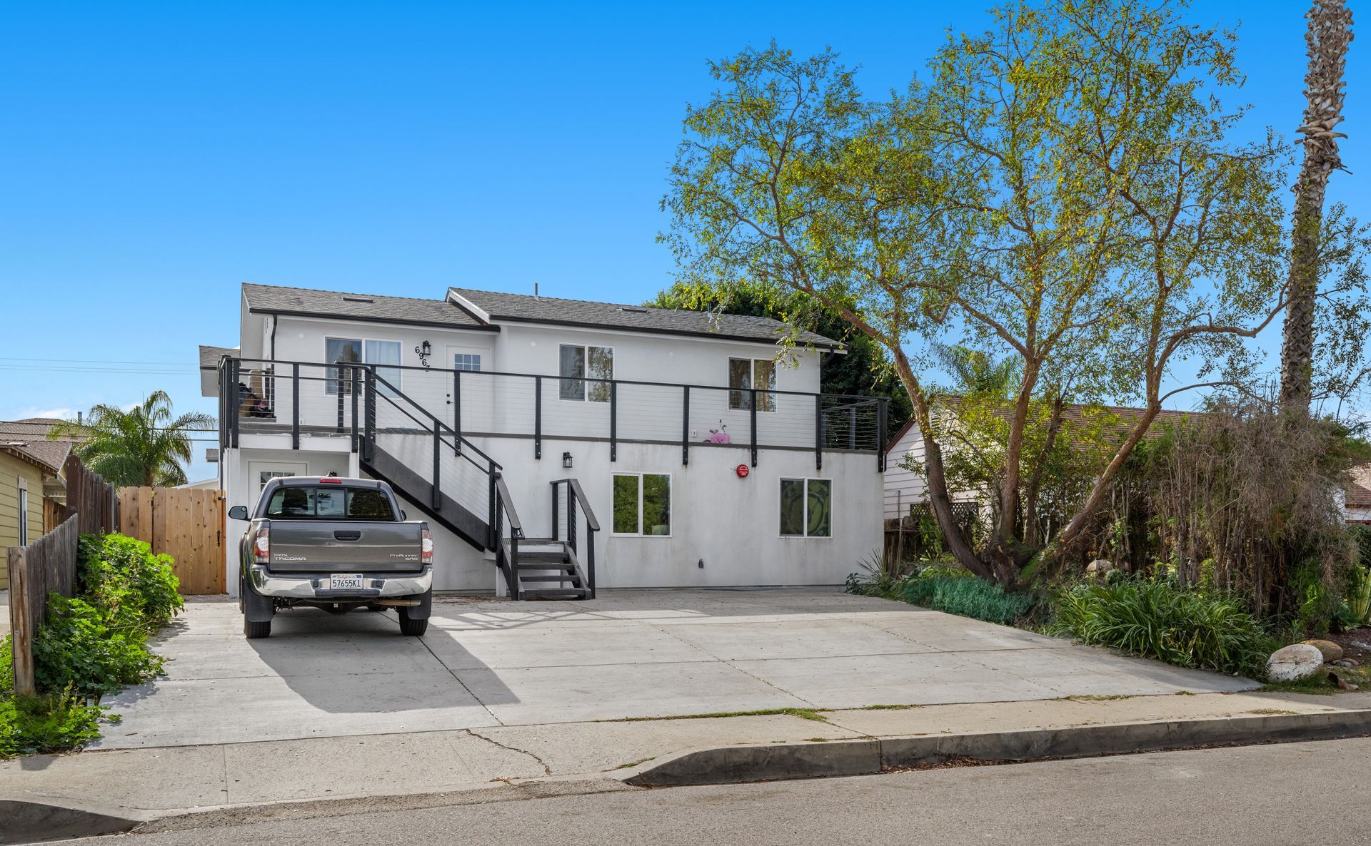 A truck is parked in front of a white house with stairs leading up to the second floor.