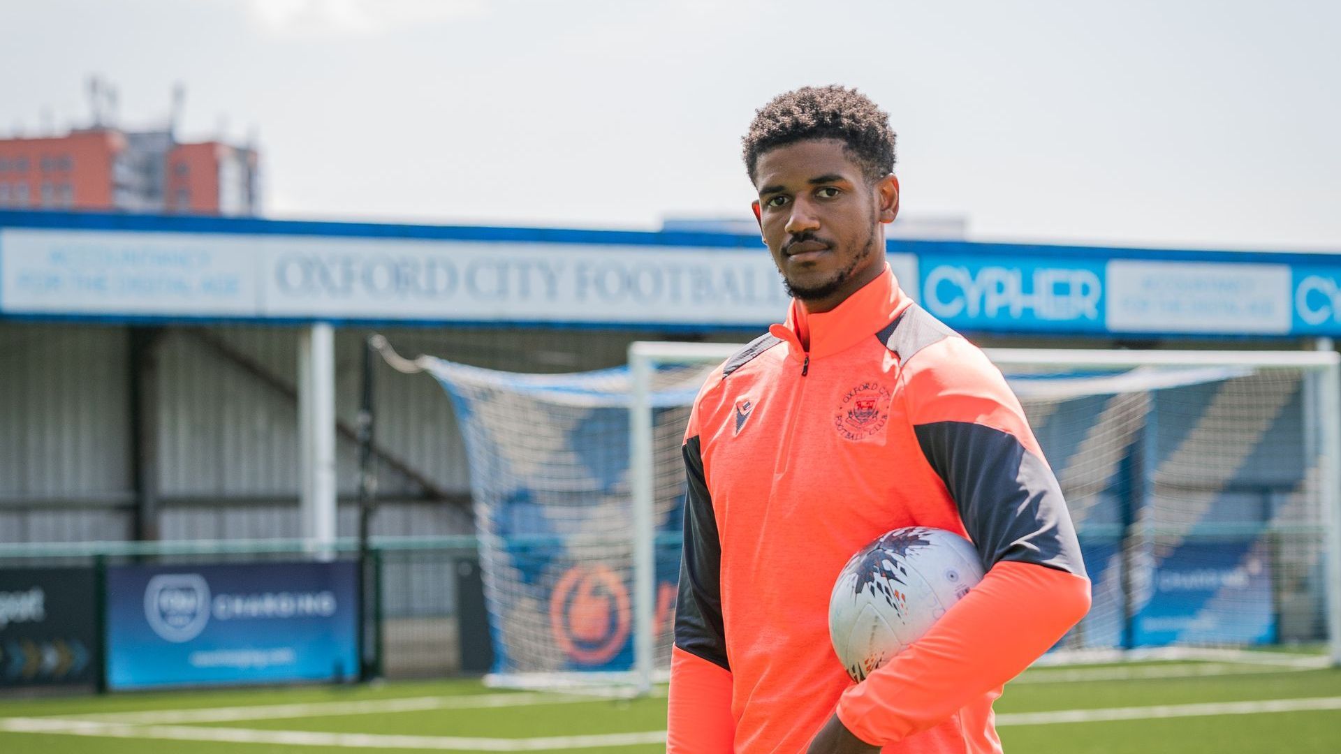 Corie Andrews holds football next to Oxford City FC sign
