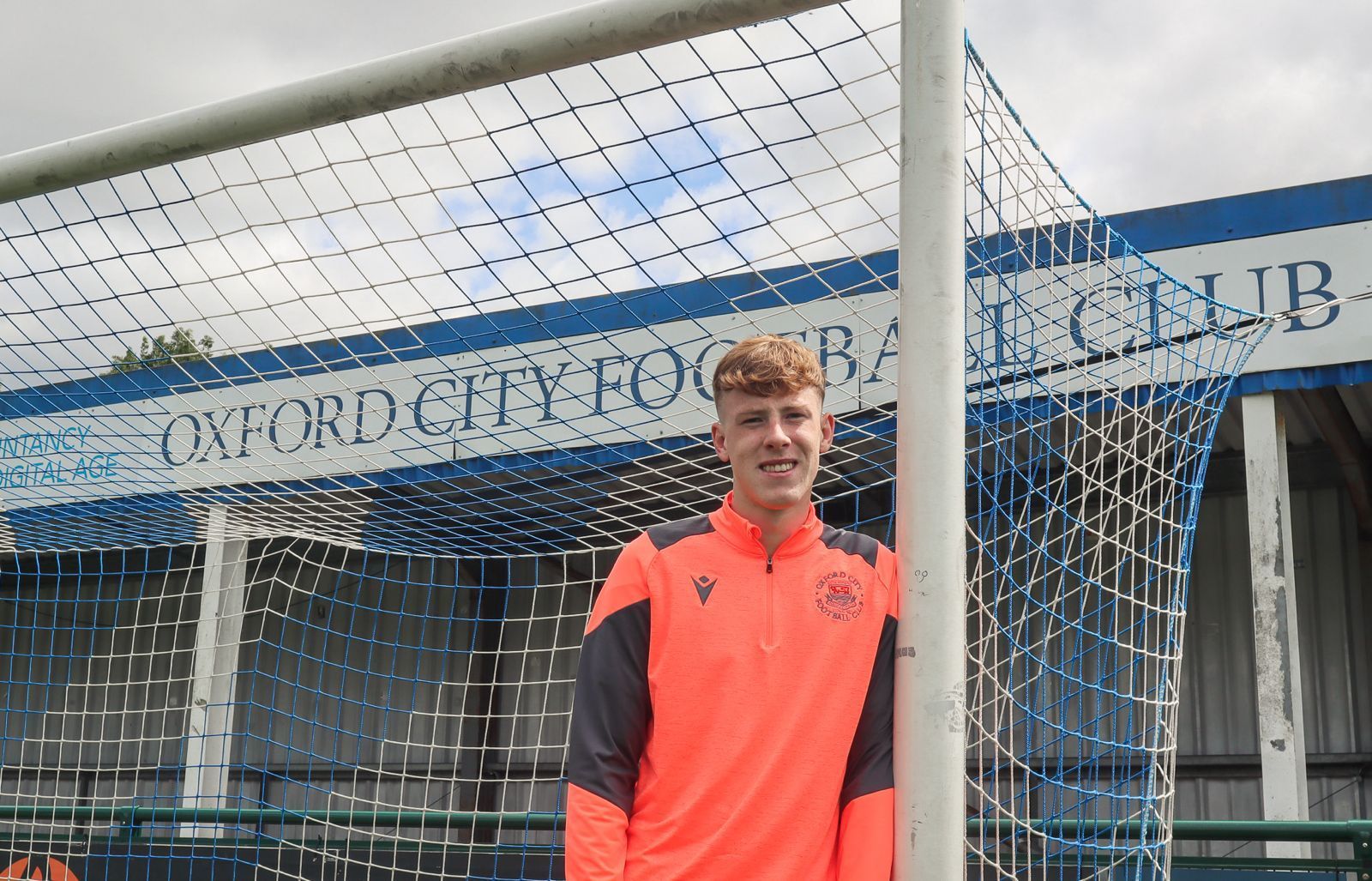 Bradley Stretton leaning on post underneath Oxford City Football Club sign