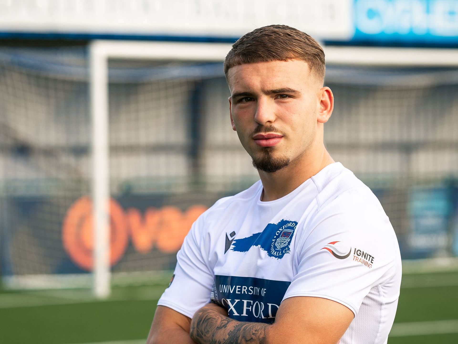 Aidan Elliott-Wheeler with arms folded in front of stand in Oxford City kit.