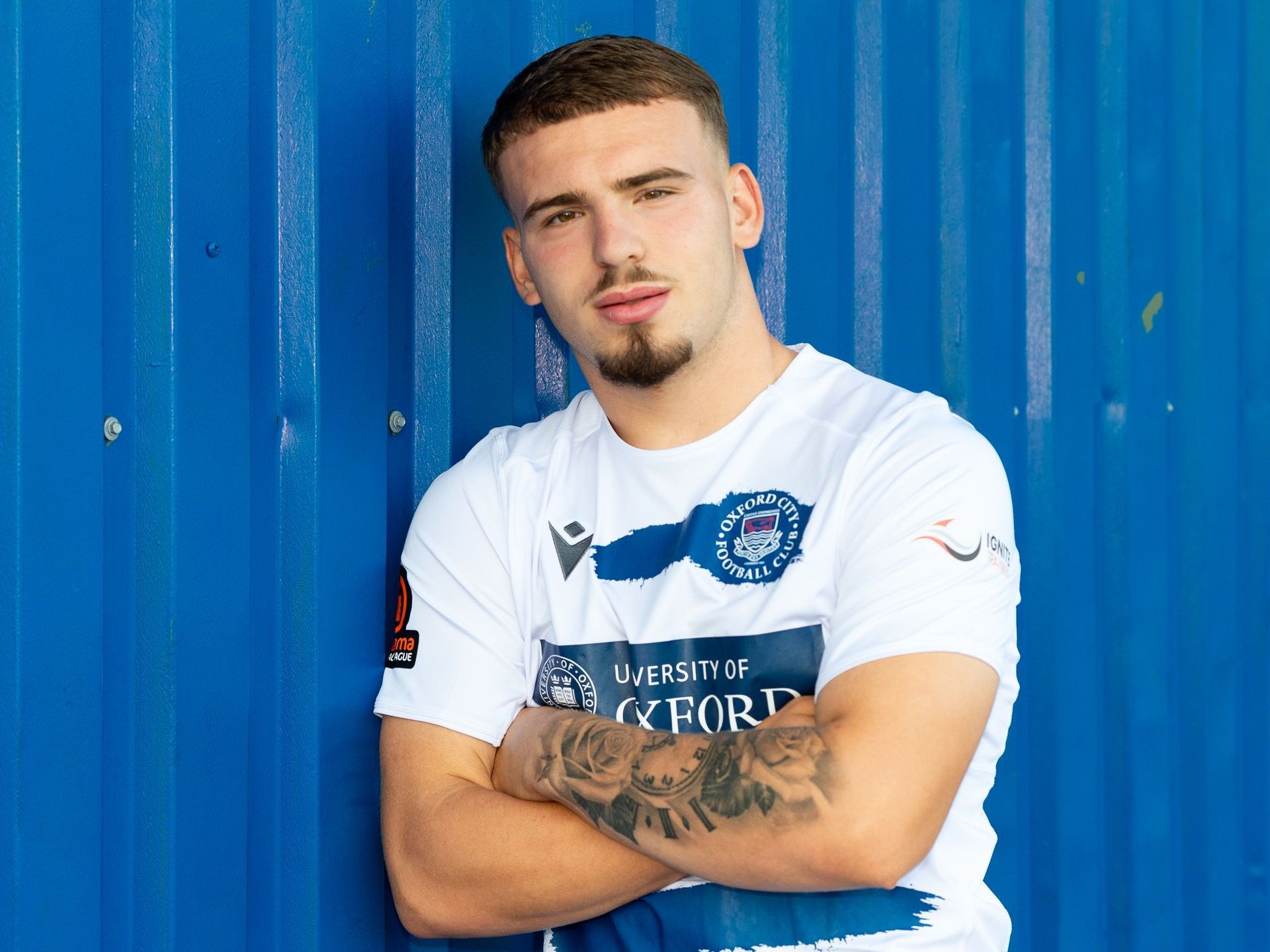 Aidan Elliott-Wheeler with arms folded leaning on blue building.