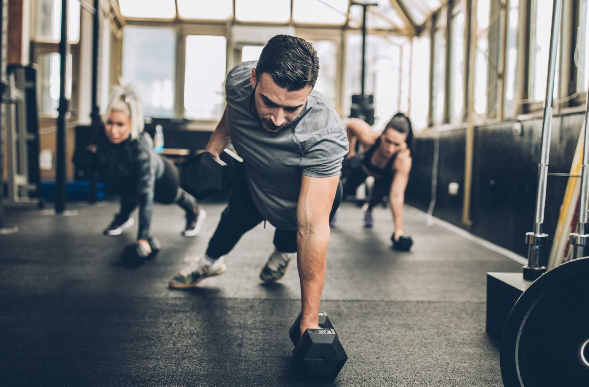 A group of people are doing push ups with dumbbells in a gym.
