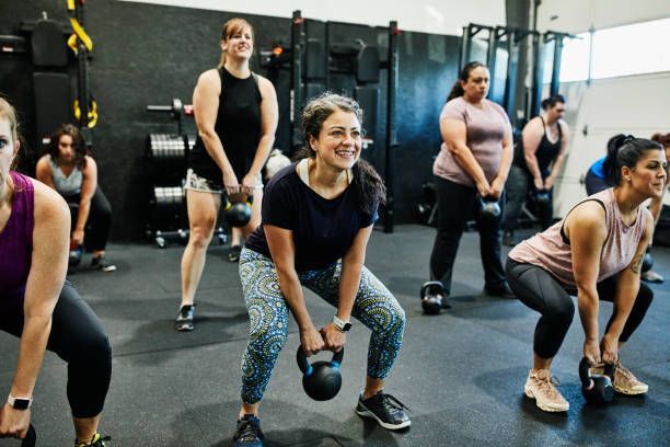 A group of women are squatting with kettlebells in a gym.