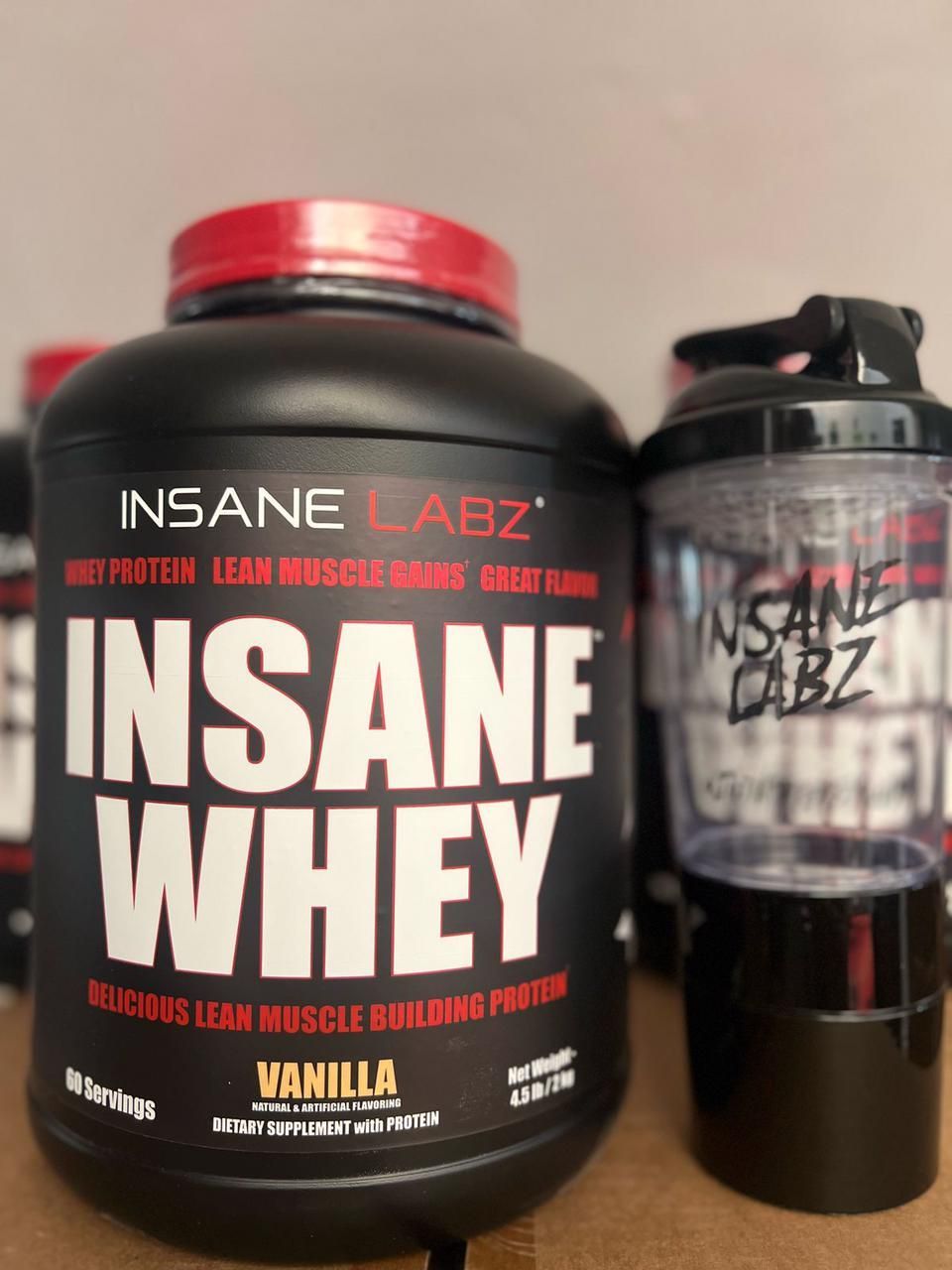 Recipiente y vaso mezclador de proteína Insane Whey de color negro con detalles rojos sobre fondo blanco.