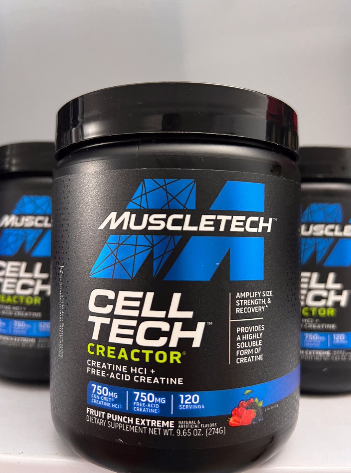 Envase de creatina Cell-Tech de Muscletech, bote negro con etiqueta azul y blanca en estante.