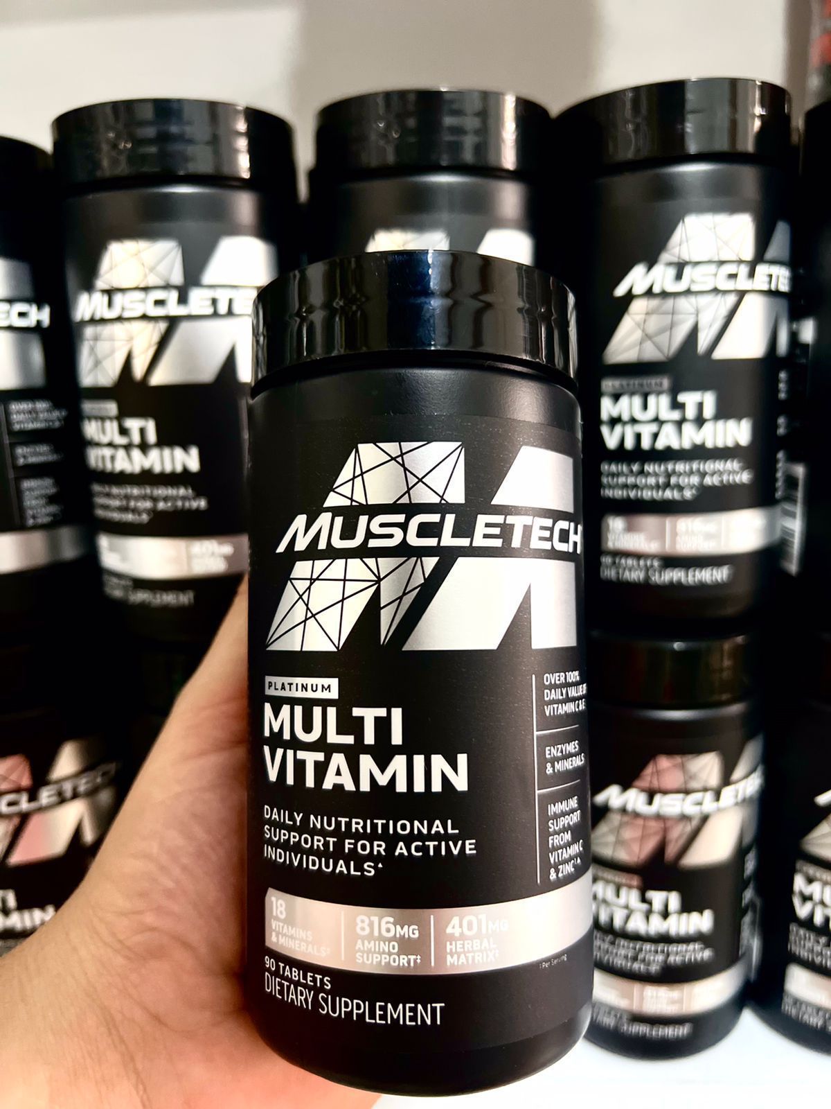 En exhibición frascos de multivitaminas MuscleTech, con etiquetas negras, texto blanco y tapas.