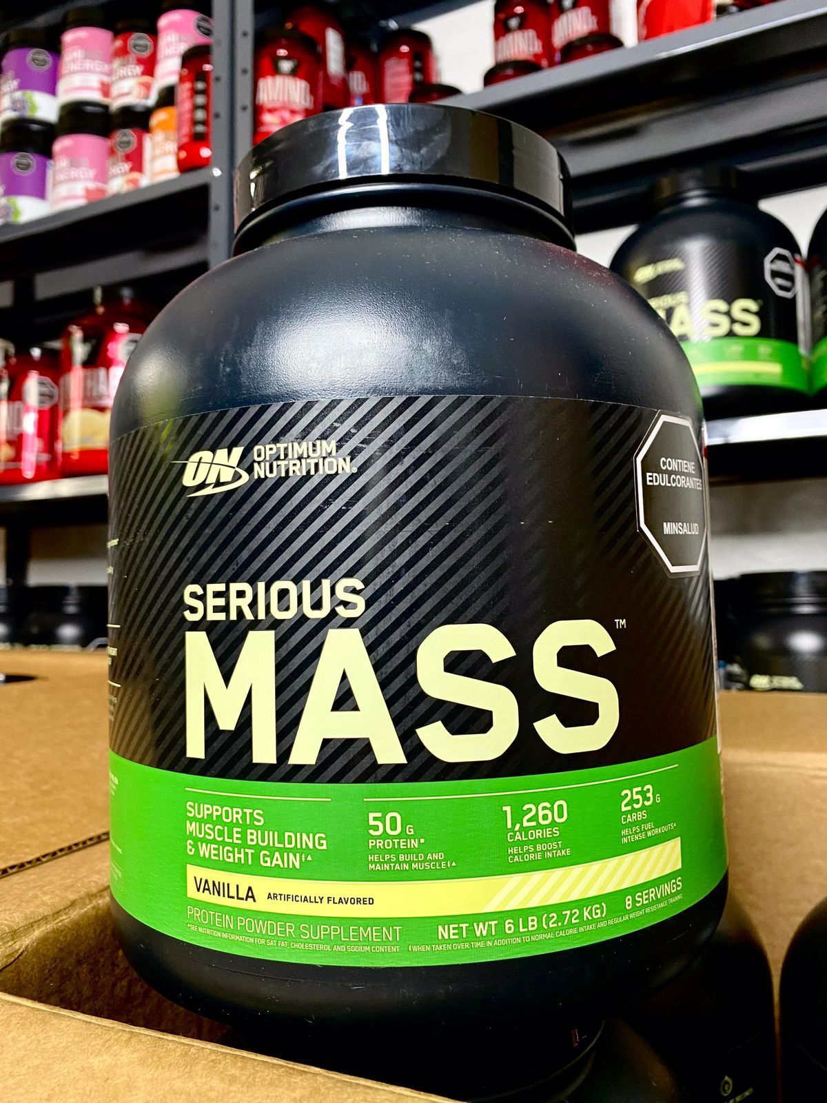 Envase de proteína en polvo Serious Mass negra con etiqueta verde en el estante de una tienda.