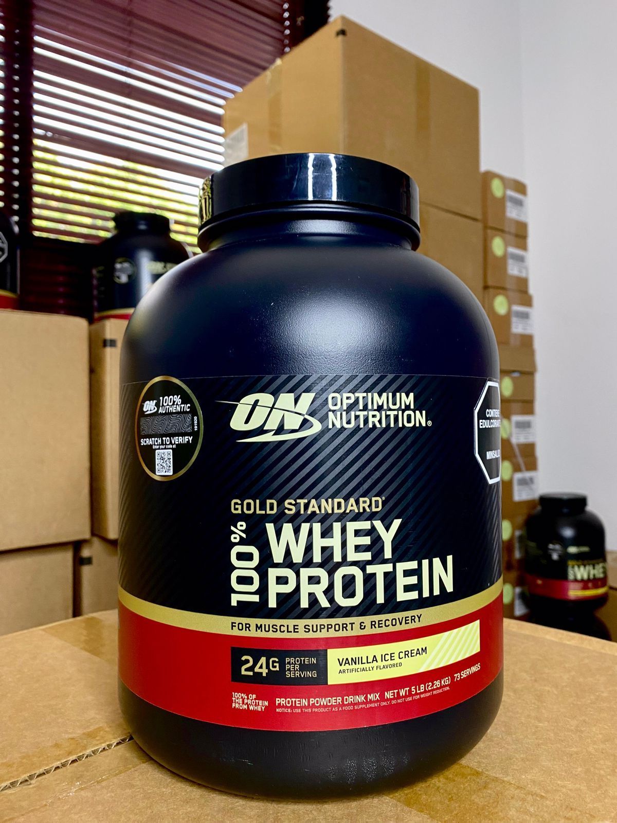 Envase negro de proteína de suero Gold Standard de Optimum Nutrition sobre una caja de cartón en el interior.