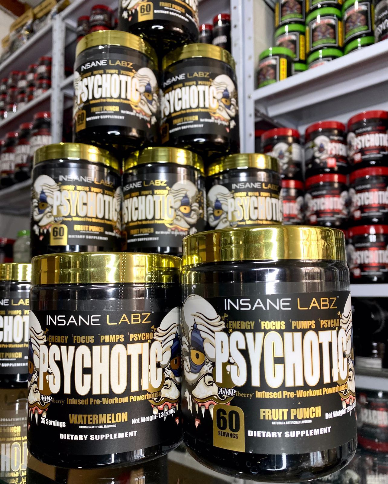 Envases apilados del suplemento PsychoTic sabor ponche de frutas en un pasillo de una tienda, con etiquetas negras y doradas visibles.