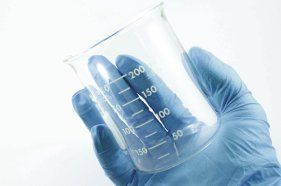 hand wearing glove holding empty beaker