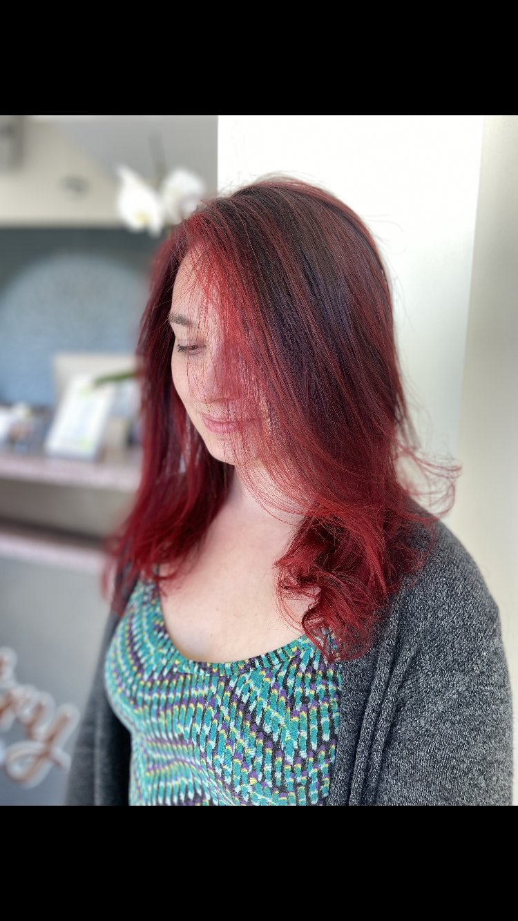 Woman with red hair and blue patterned top, in a salon setting.