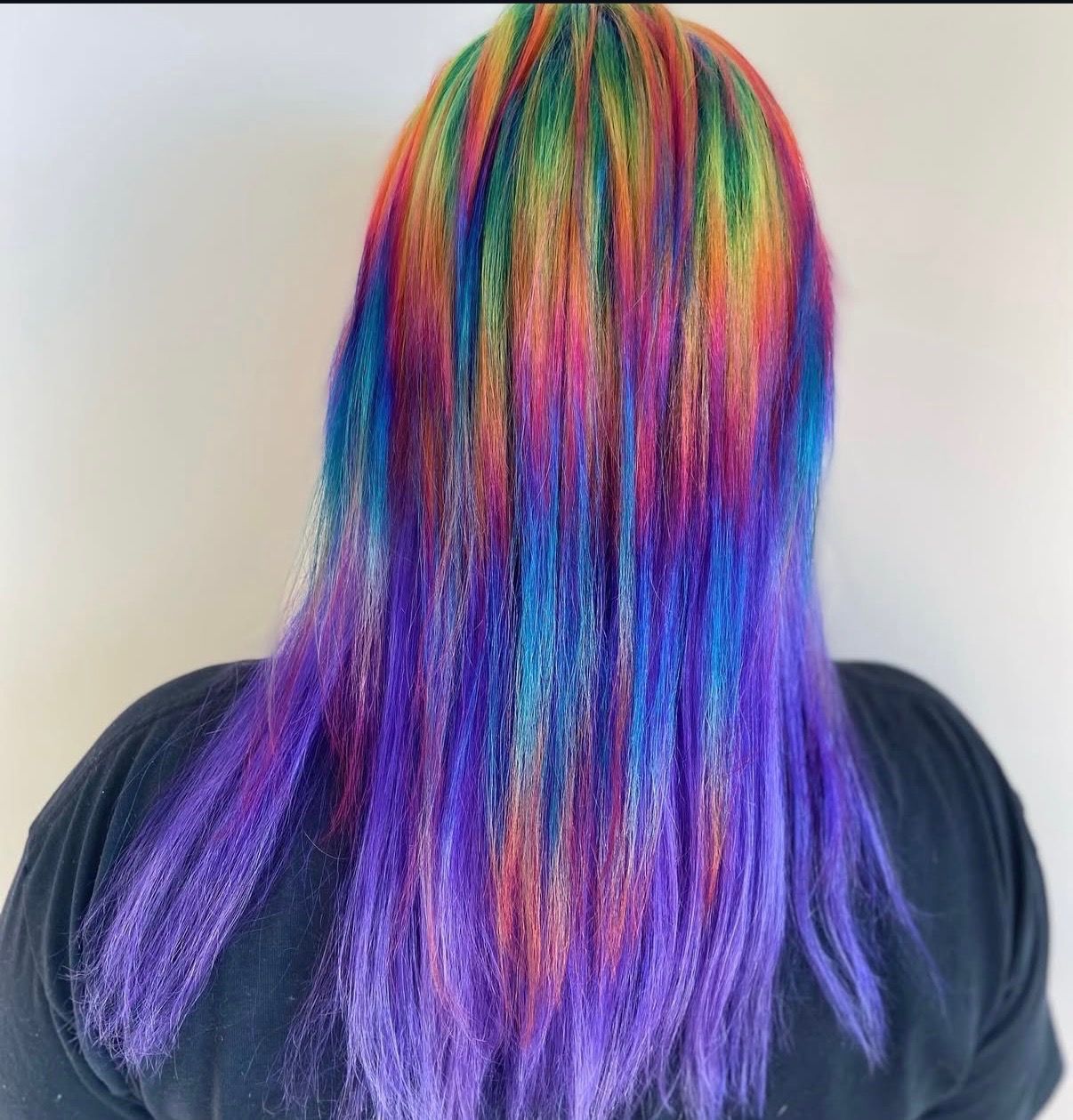 Person with long hair dyed in a rainbow of colors, including purple, blue, green, yellow, and red.