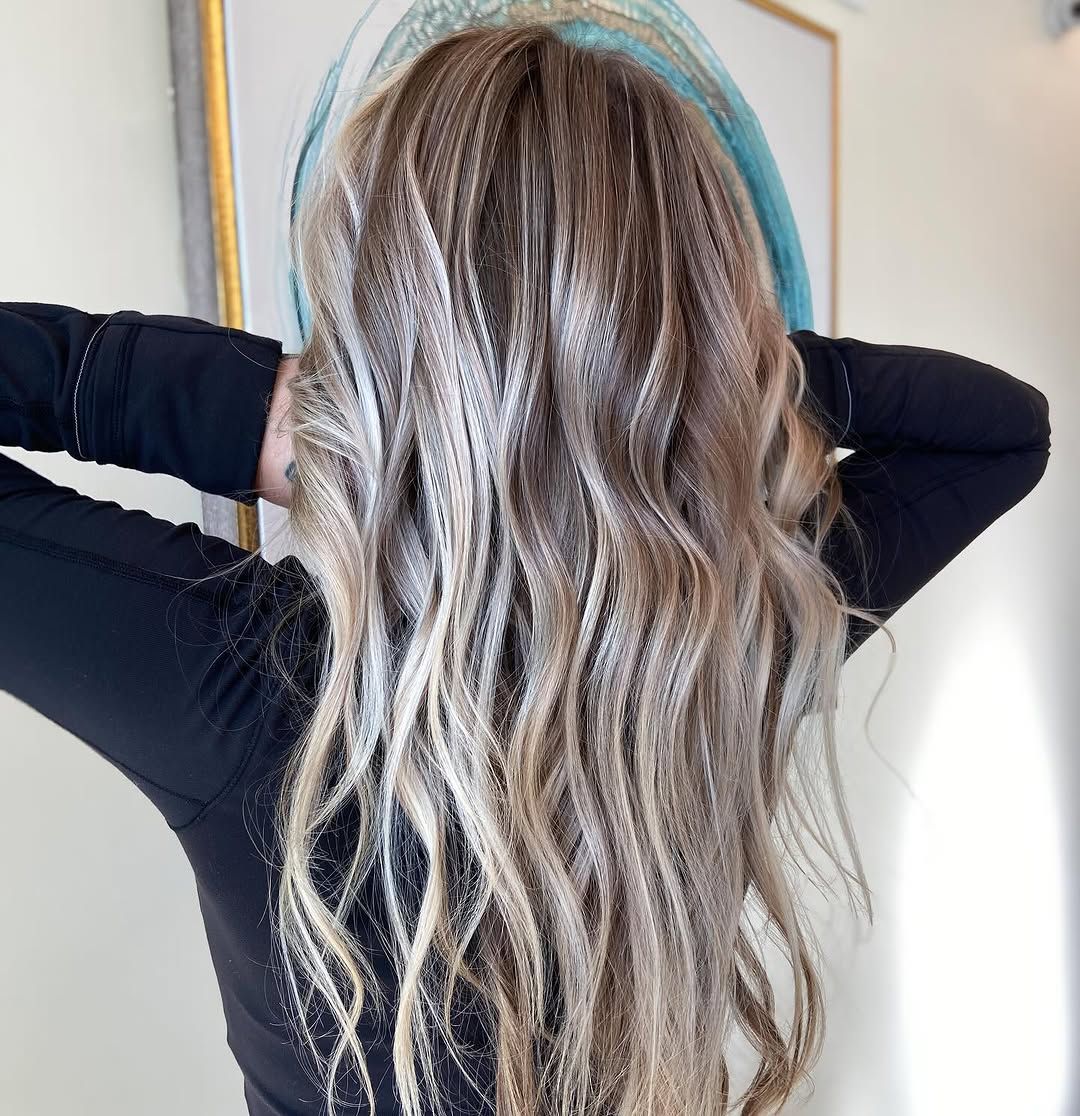 Woman with curled ash- blonde hair, arms raised behind her head, wearing a black top.