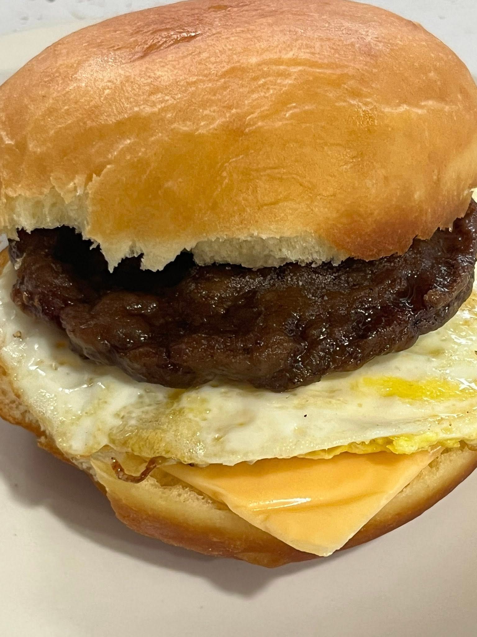 A close up of a hamburger with eggs and cheese on a bun on a plate.