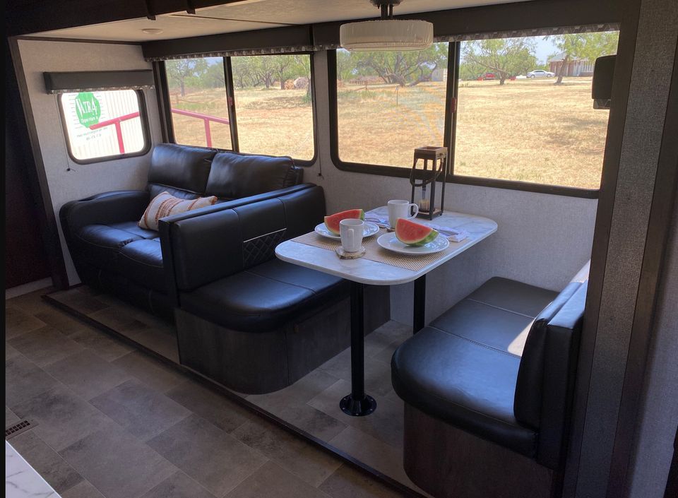 Modern RV interior featuring a black couch and a dining table with plates and fresh watermelon.