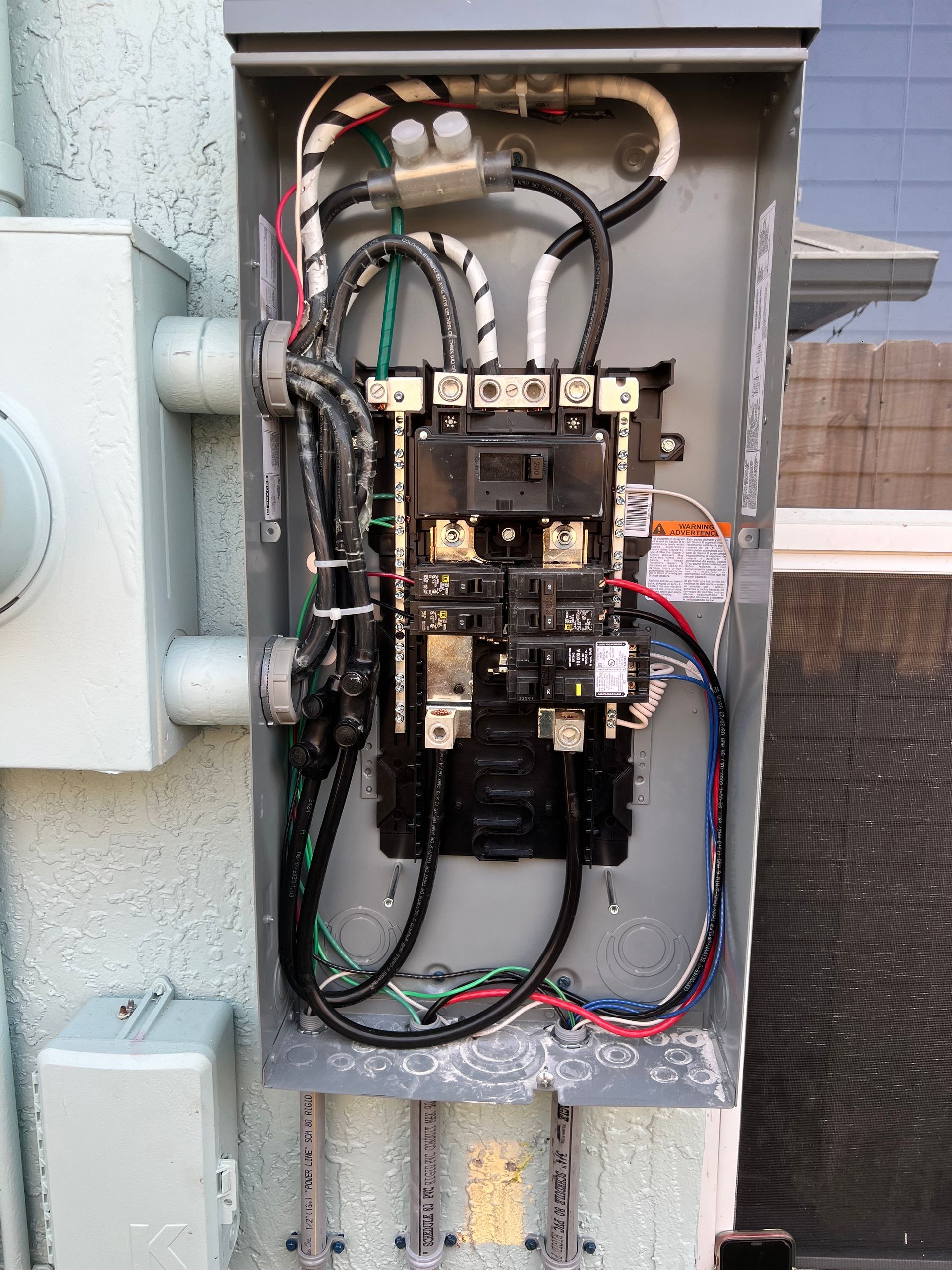 Electrical panel mounted on an outdoor wall, showing wires and circuit breakers.