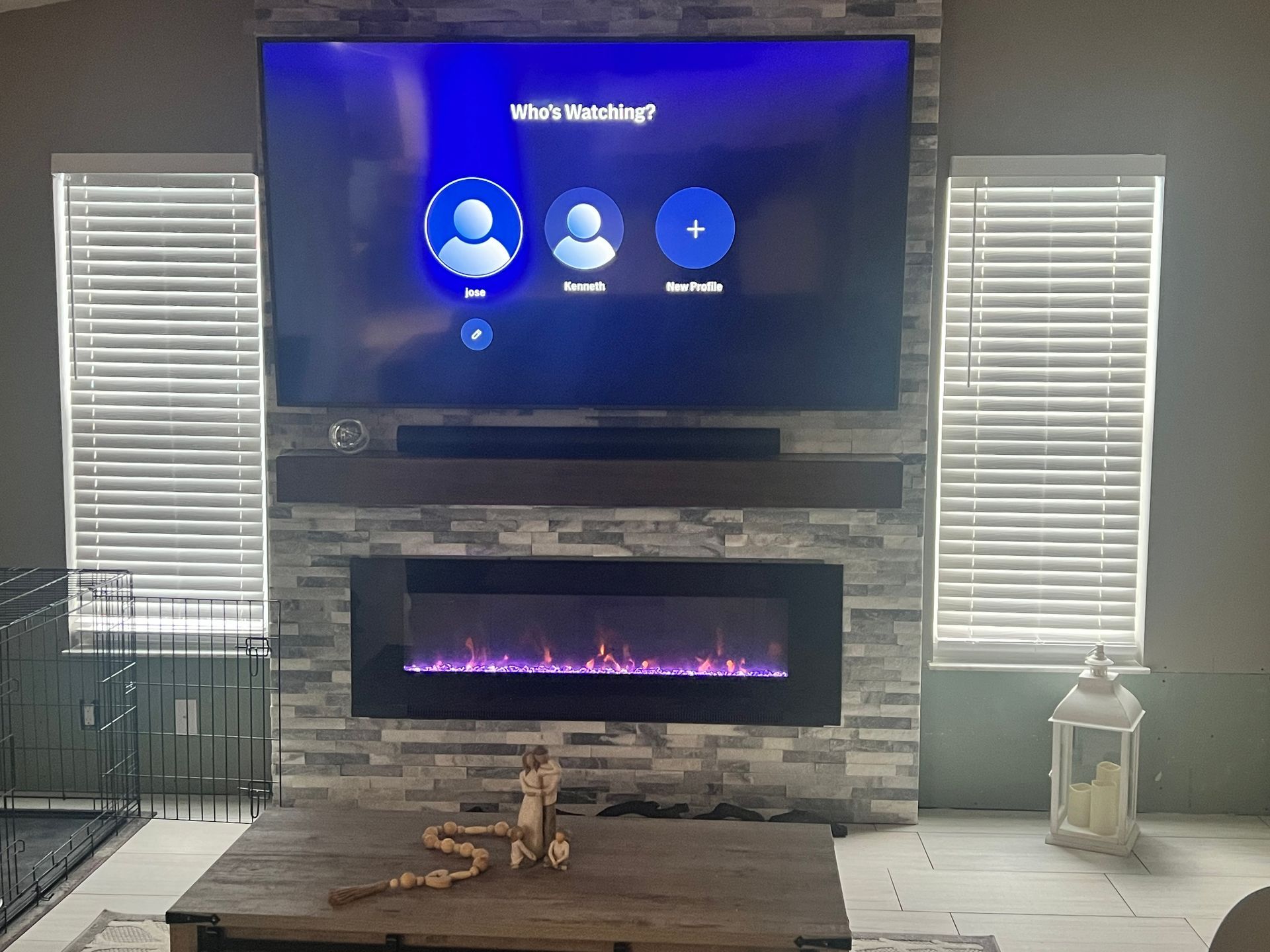 Living room with TV above fireplace, stone accent wall, blinds, and a coffee table.