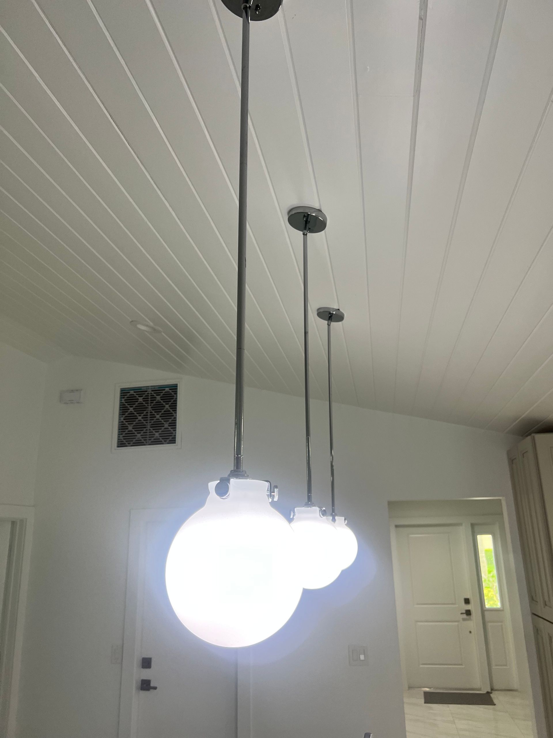 Three pendant lights with round white globes hanging from a white slatted ceiling.