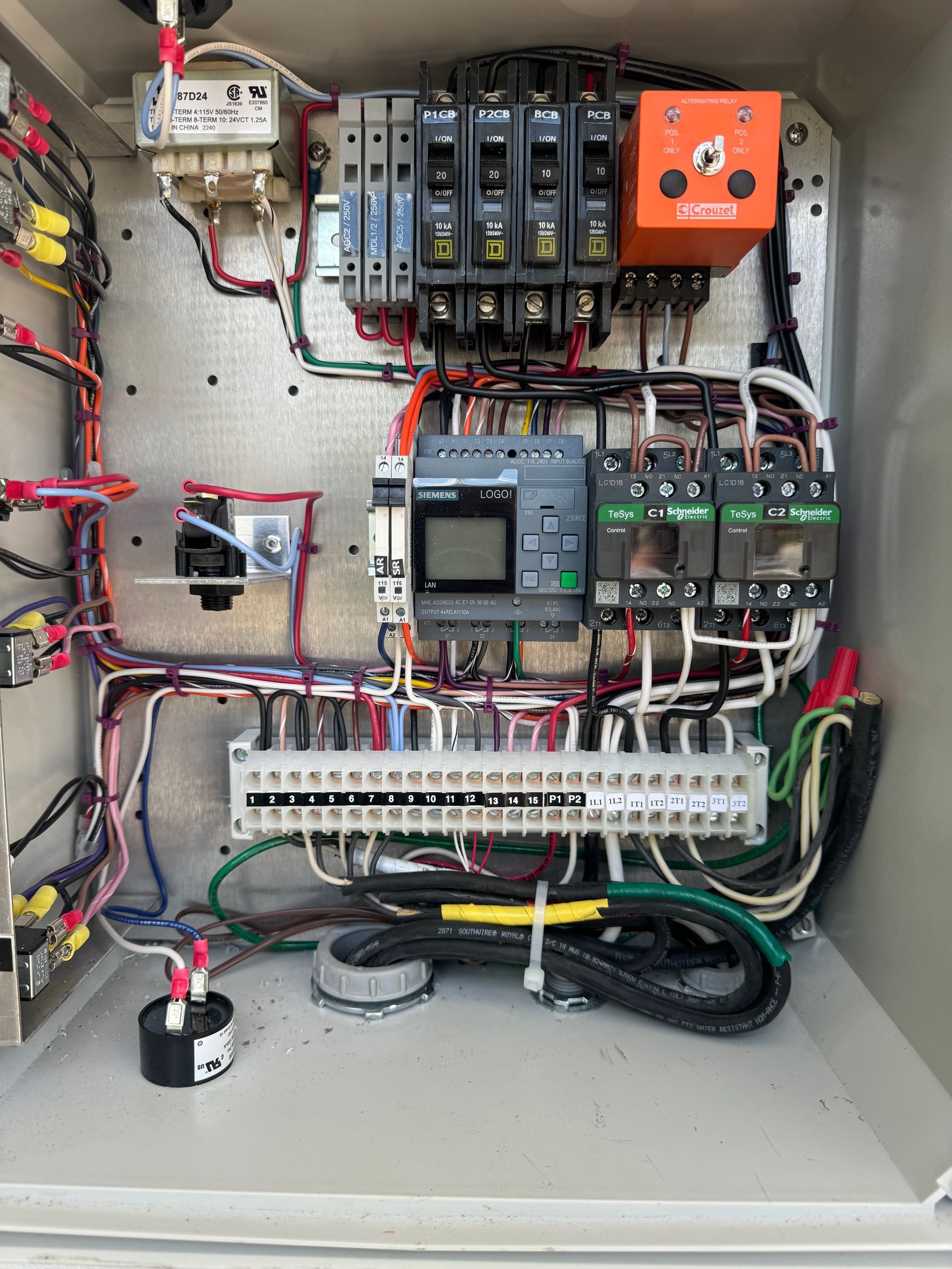 Electrical control panel with wires, breakers, and a PLC in a metal enclosure.