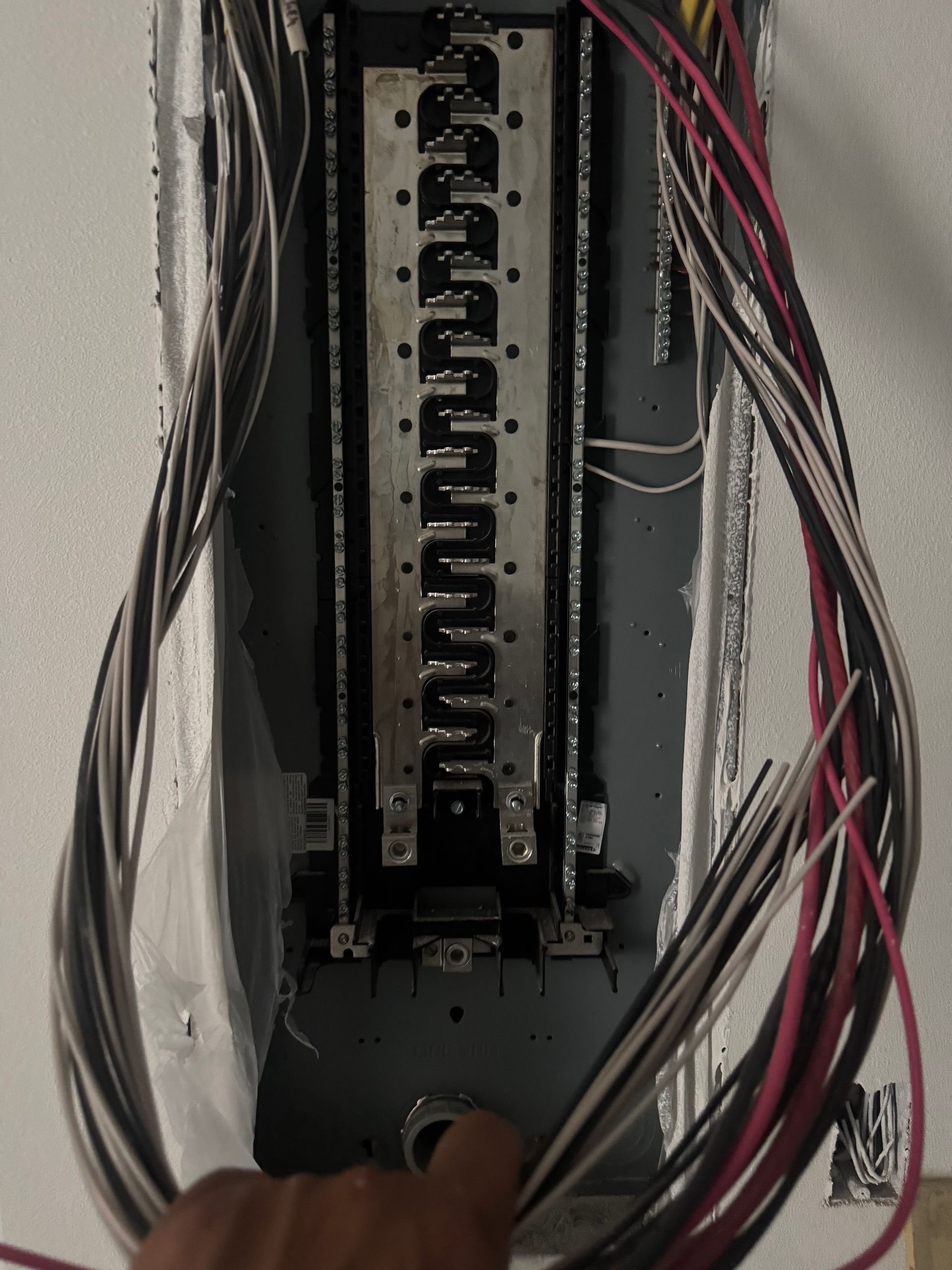 Electrical panel with wires; a hand points toward the bottom.