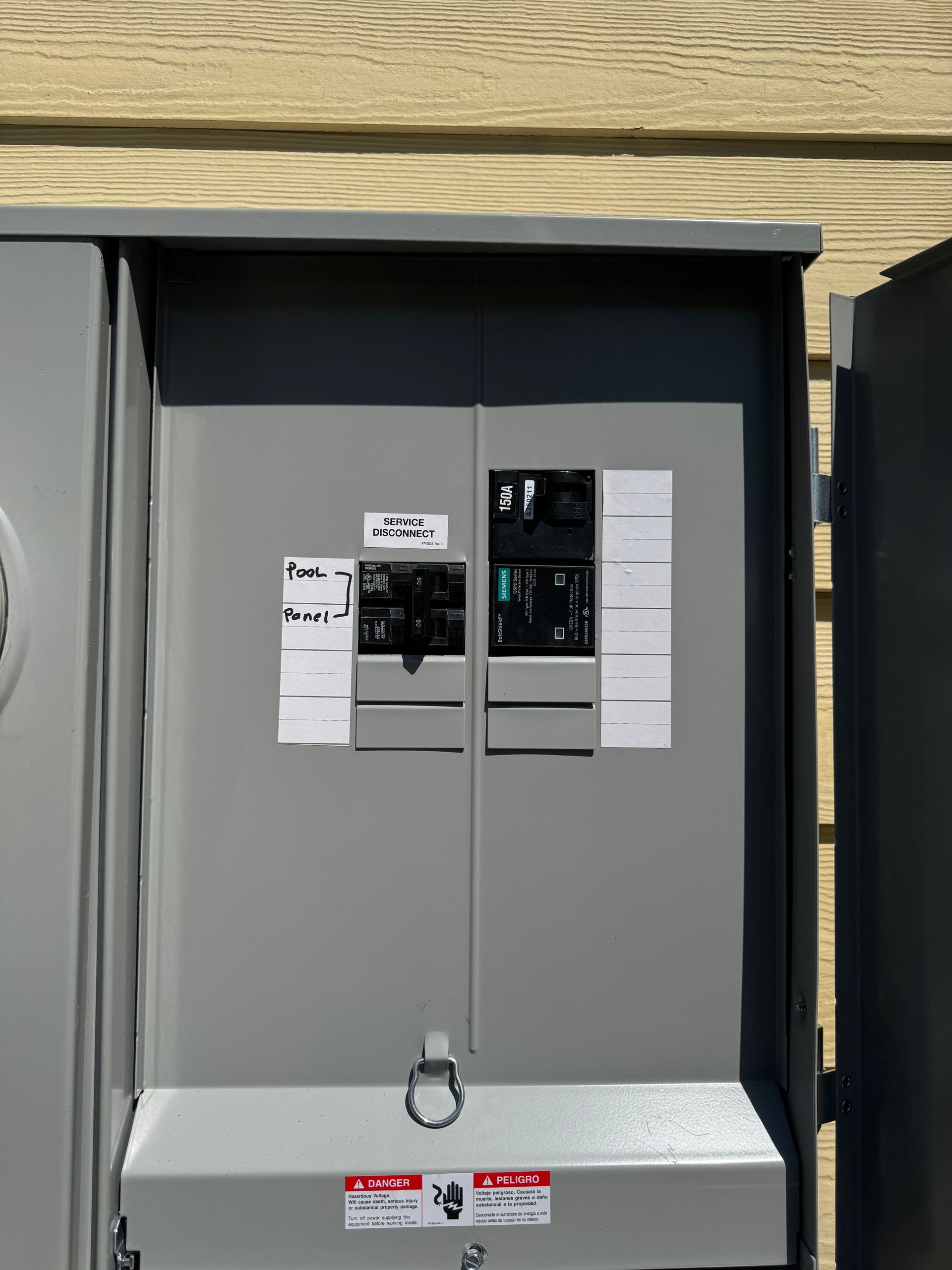 Gray electrical panel with two closed doors and labels, mounted on a yellow-brown siding.