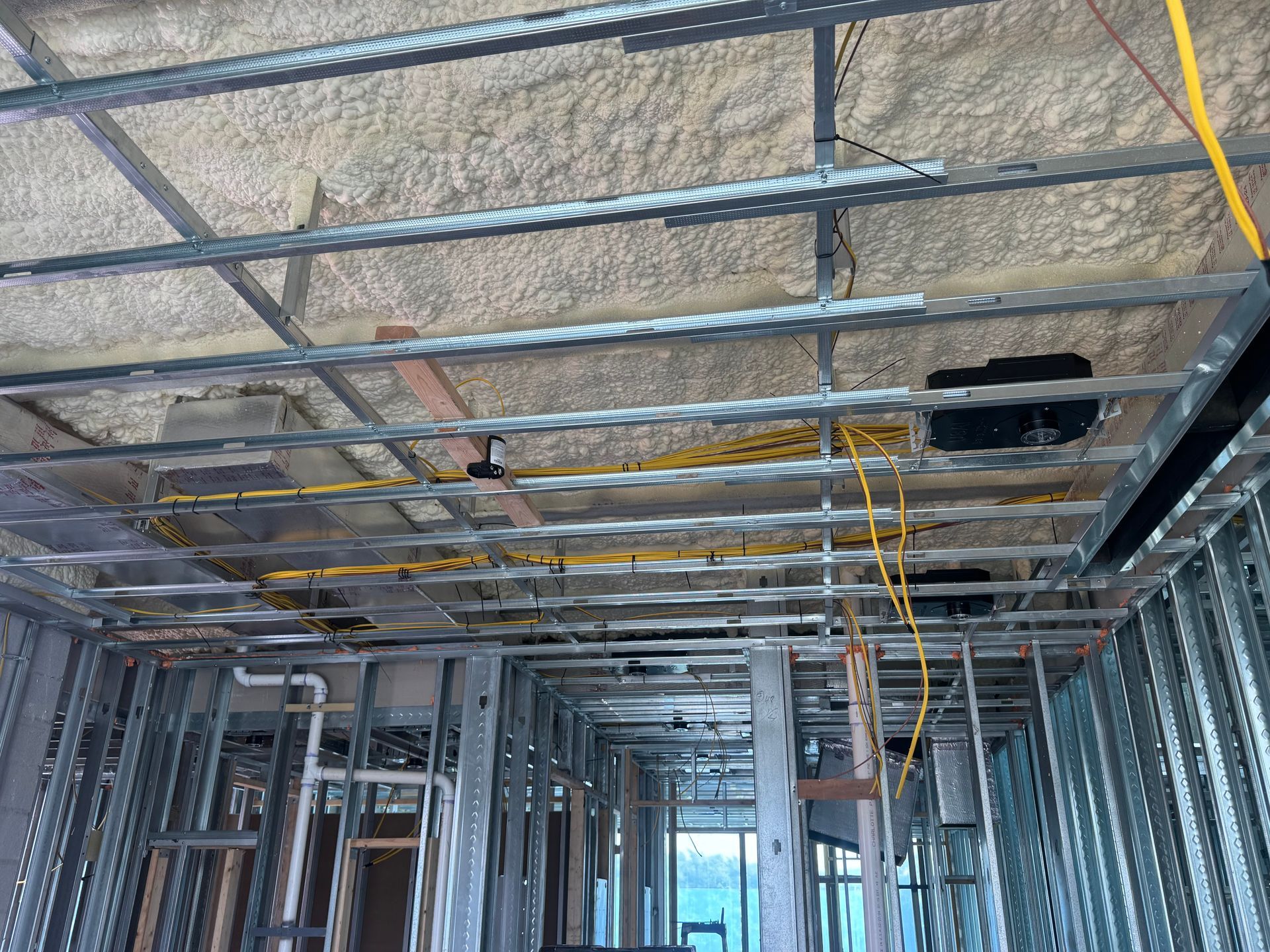 Interior view of a building under construction, showing metal framing and exposed wiring. Insulation sprayed on ceiling.