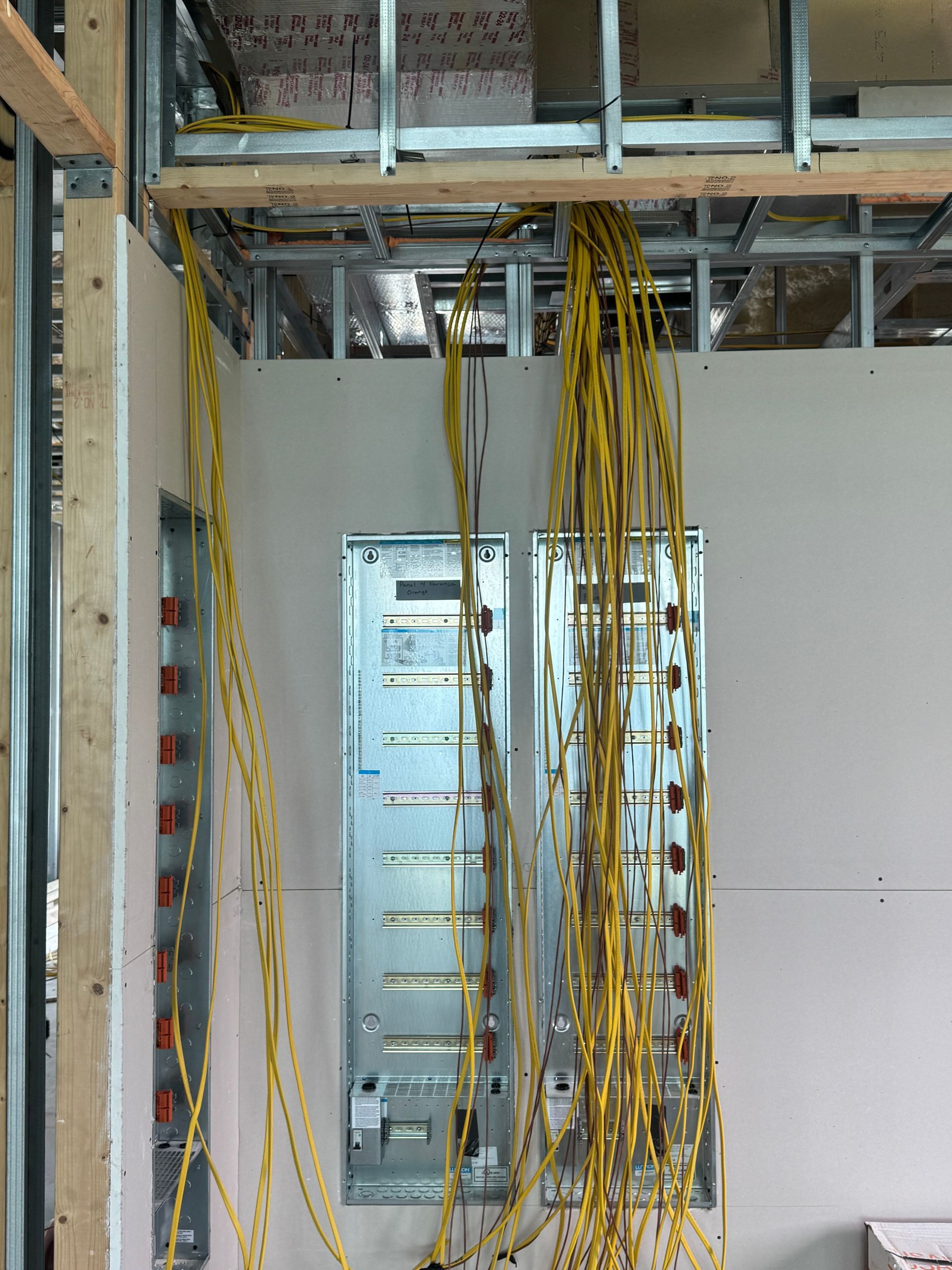Electrical wiring installation inside a building frame. Yellow wires hang from the ceiling towards electrical panels in the wall.