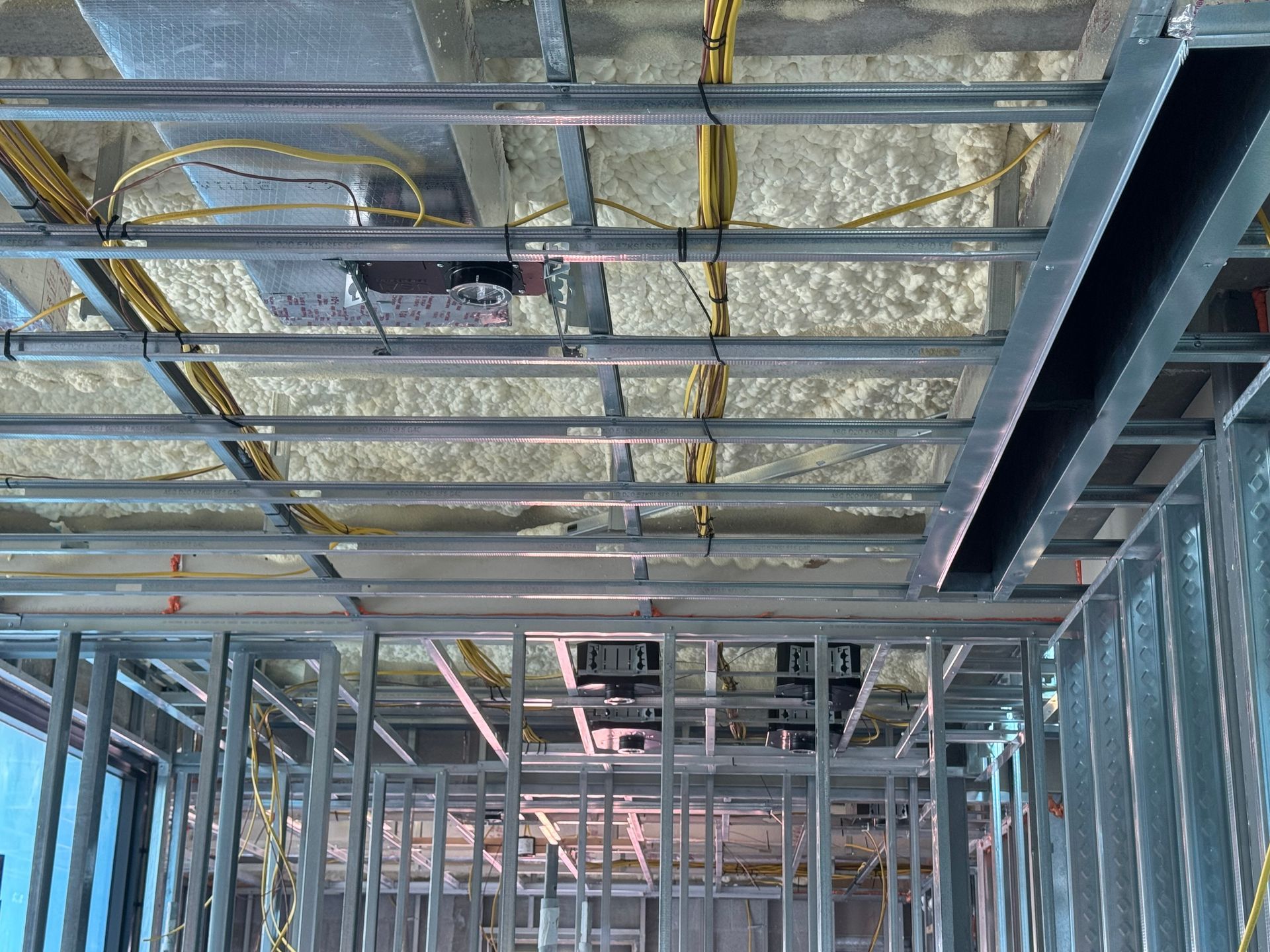 Metal framing for a building's ceiling and walls, with exposed wiring and insulation.