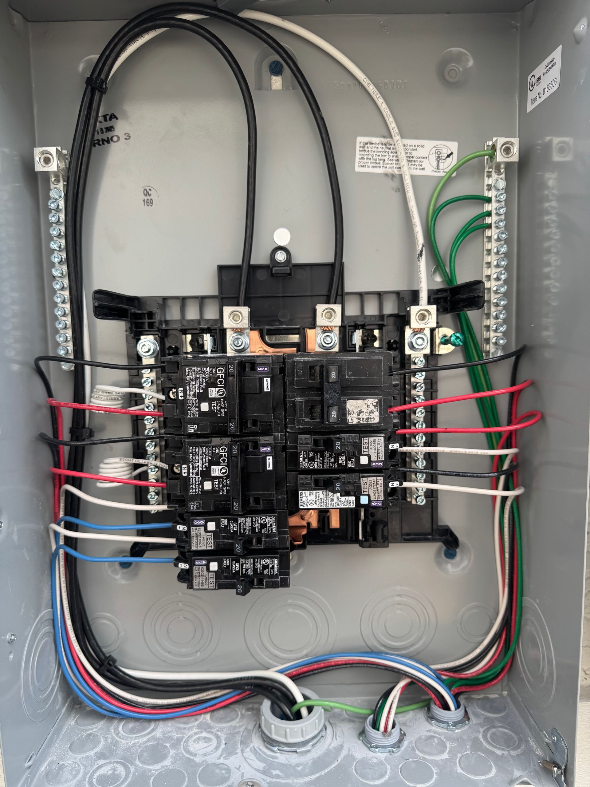 Electrical panel with wires and circuit breakers. Gray metal box, black, red, white, blue, and green wires.
