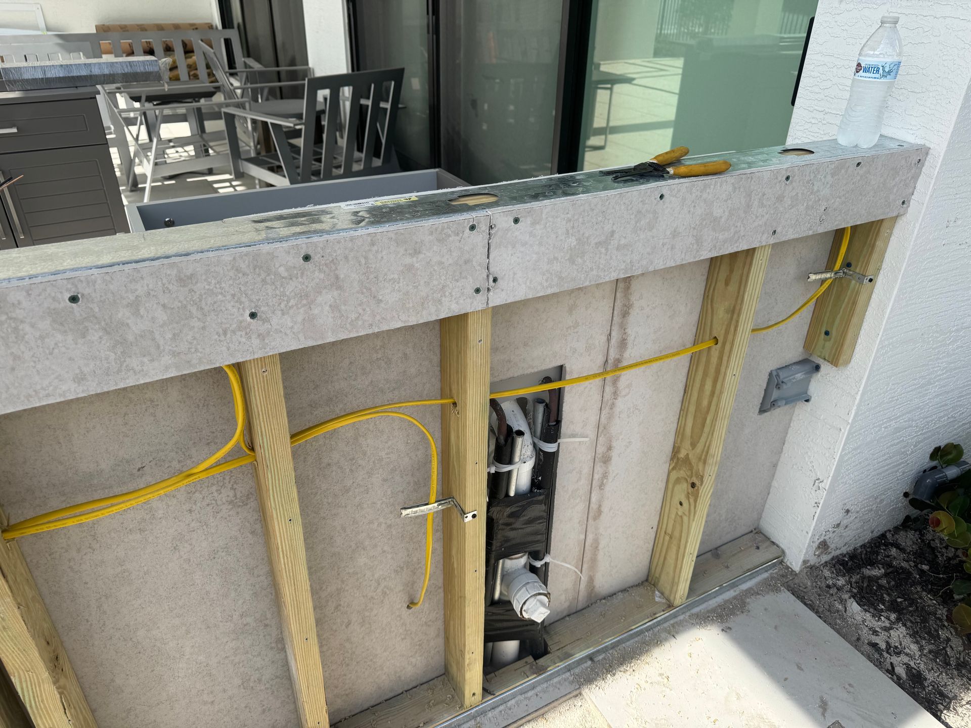 Outdoor bar under construction: wooden frame, electrical wiring, gray countertop, and white exterior wall.