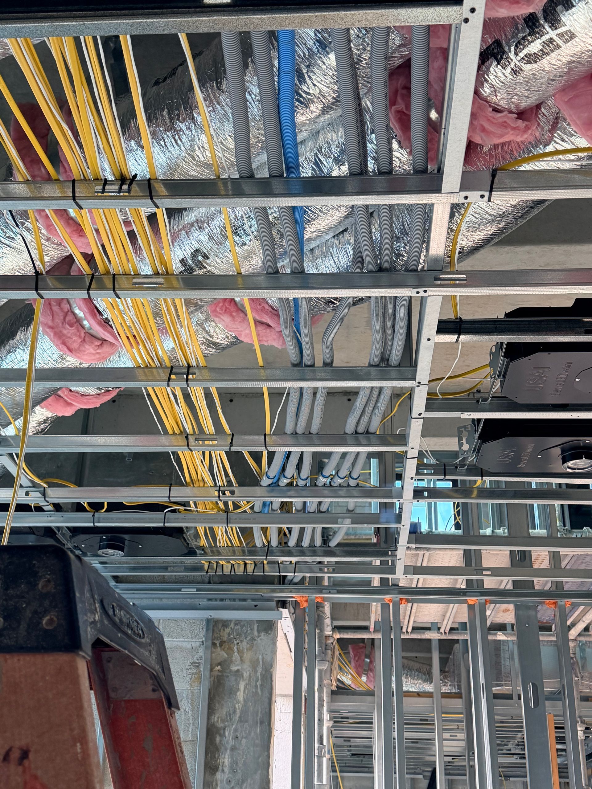 Electrical wiring and insulation above a metal frame ceiling, construction site.