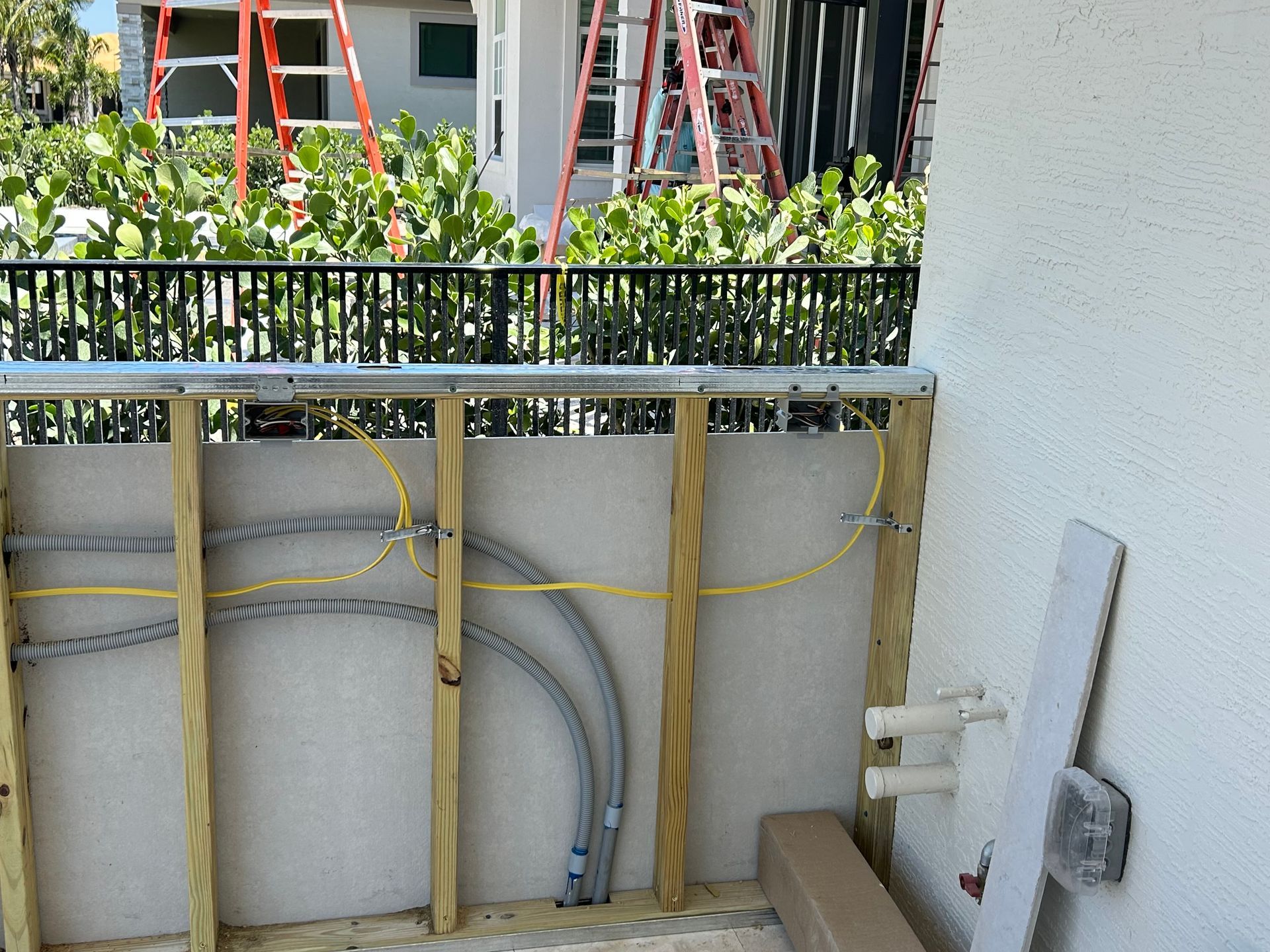 Construction site: wooden frame, electrical wiring, metal railing, cactus and ladders in background.
