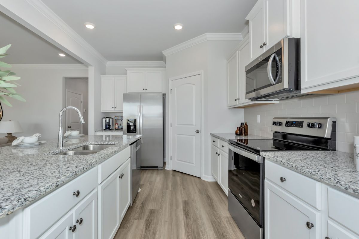 White kitchen with granite countertops, stainless steel appliances, and light wood flooring.