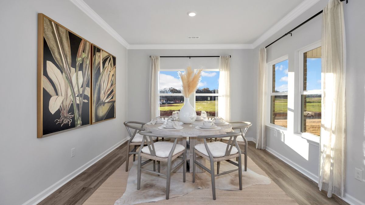 Formal dining room with round table, six chairs, art, windows, light colors, and rug.