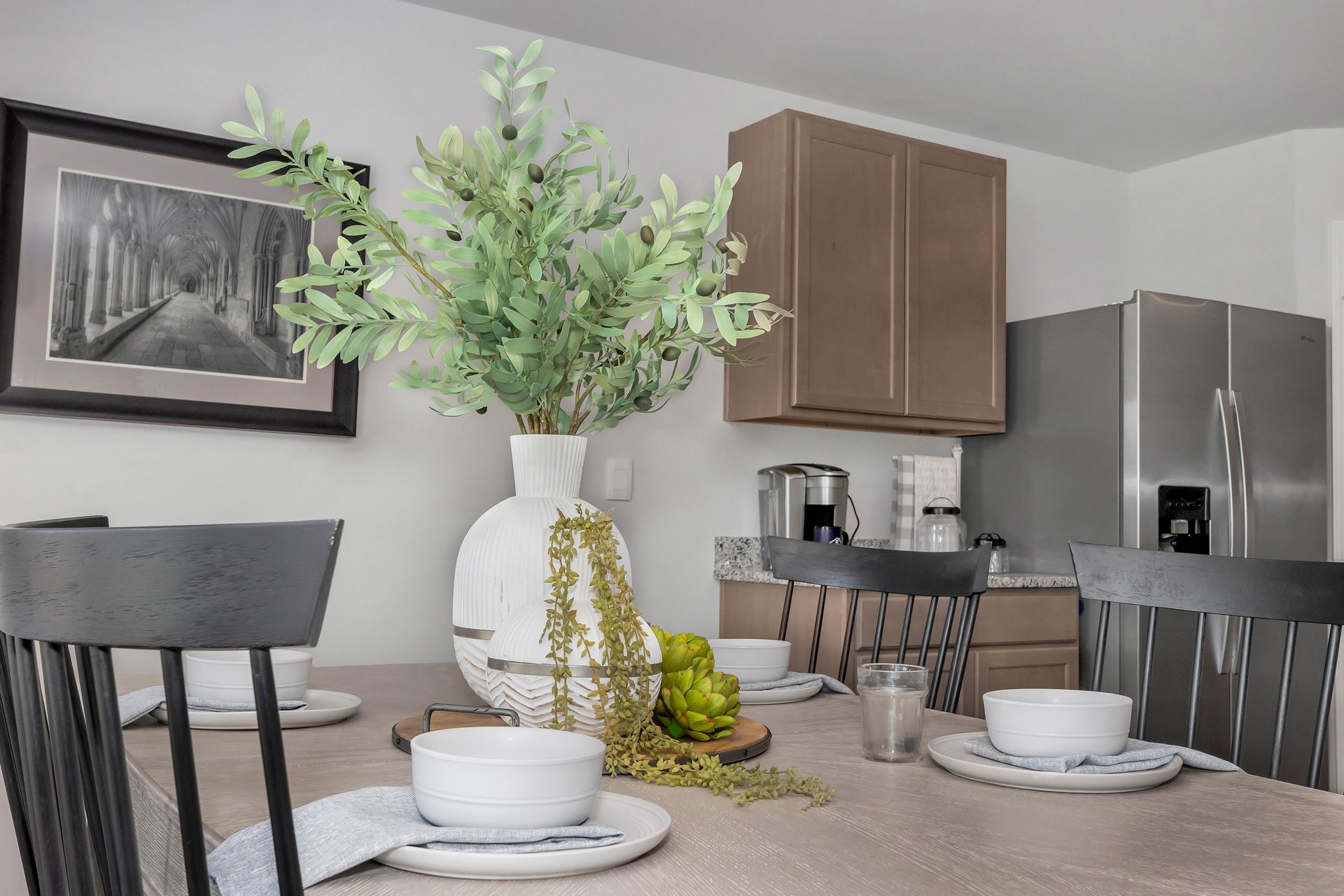 Dining table set with white bowls, vase of greenery, and a framed picture.