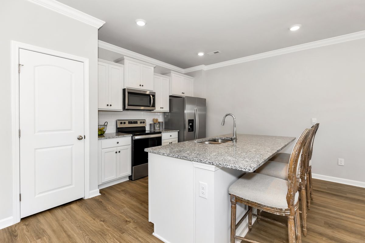 White kitchen with island and stools, stainless steel appliances, and light-colored flooring.