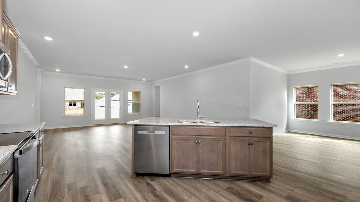 Spacious, empty kitchen with island, stainless steel appliances, and light wood floors.