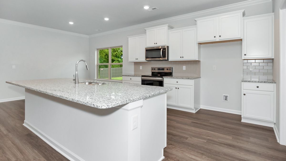Modern kitchen with white cabinets, granite island, stainless steel appliances, and wood flooring.