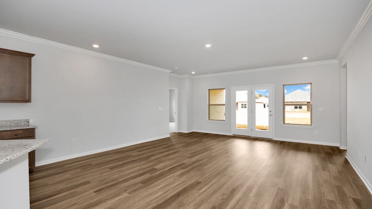 Empty, bright living space with wood flooring and white walls, windows, and a door.