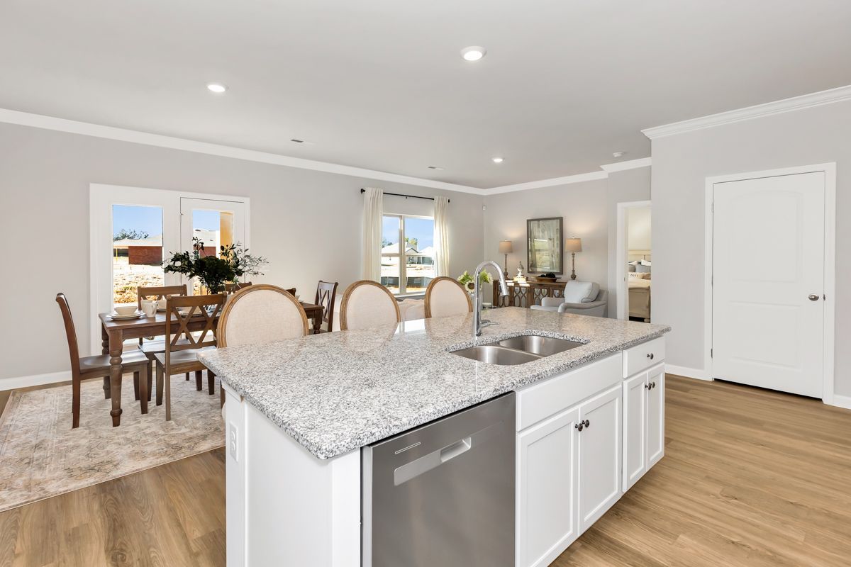Bright, open-concept kitchen with island and granite countertop, leading into a dining area with a window.