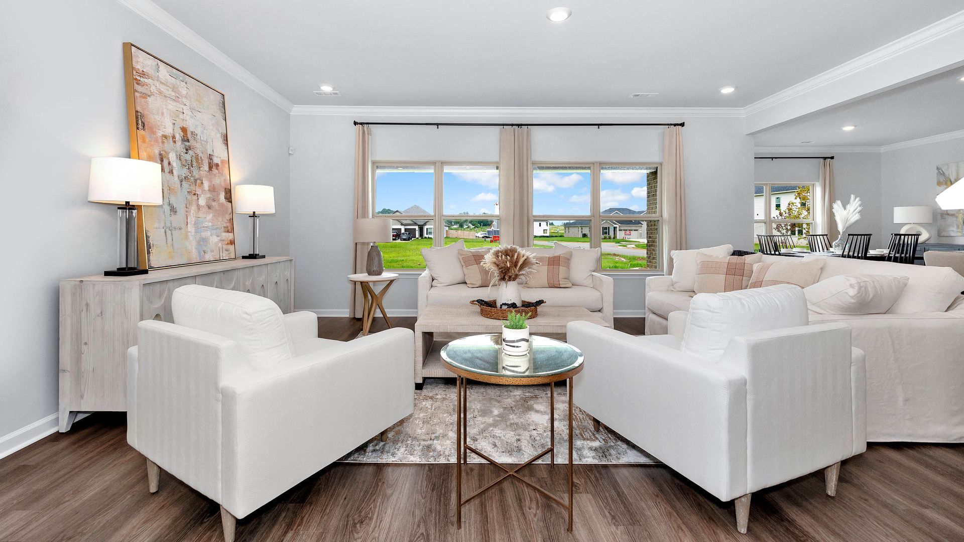 Living room with white furniture, neutral colors, and large windows overlooking a green lawn.