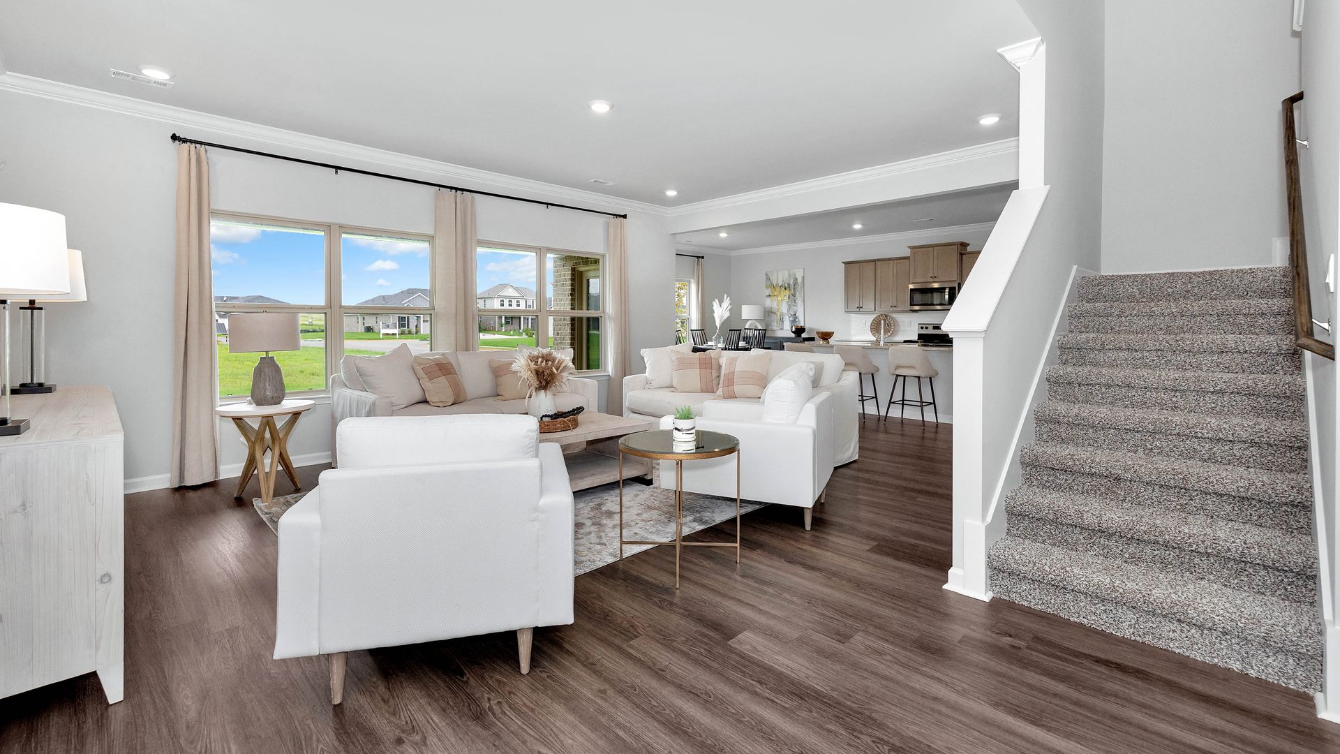 Bright living room with white sofas, hardwood floors, and staircase.