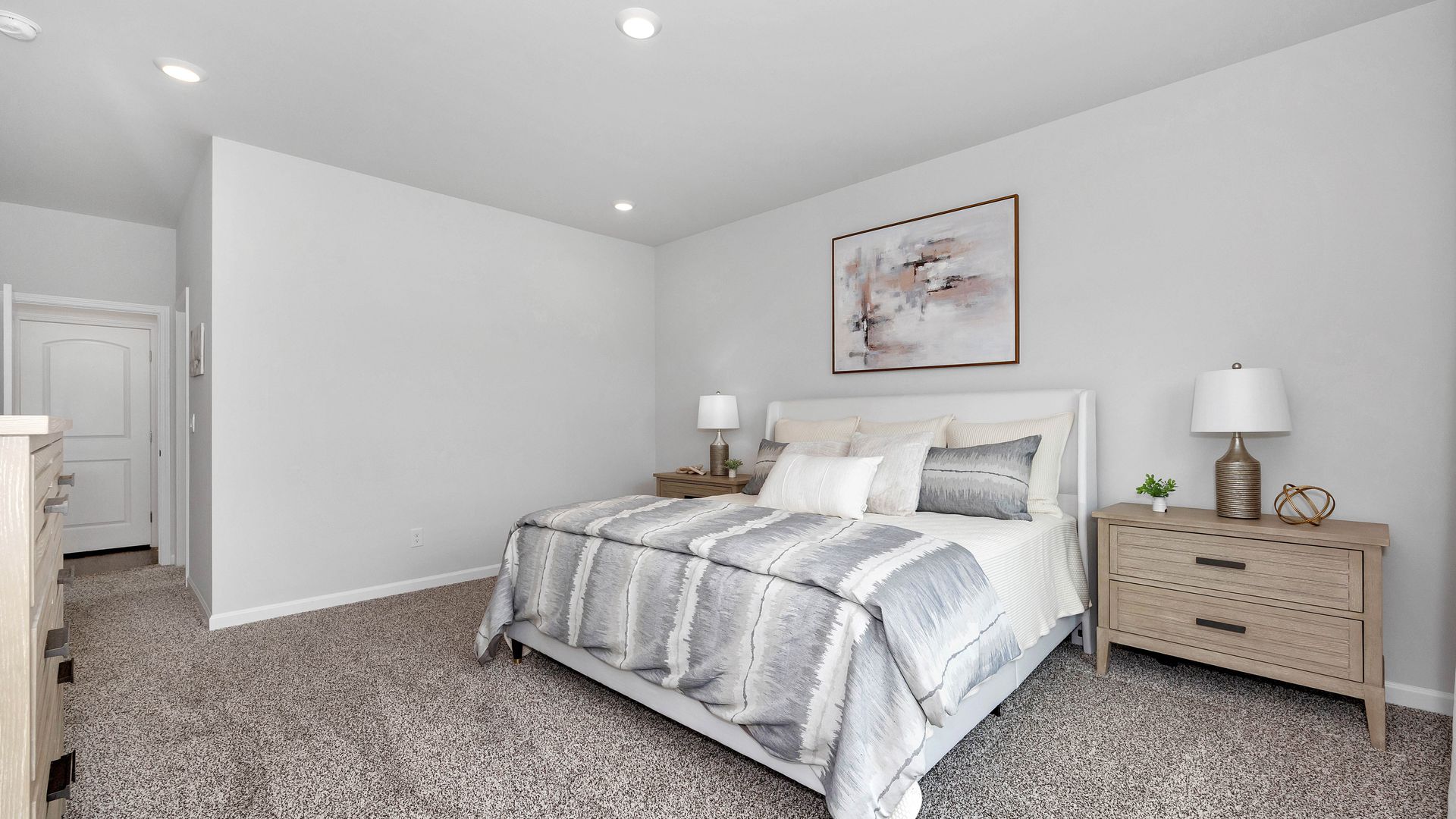 Bedroom with bed, nightstands, artwork, and neutral carpet.