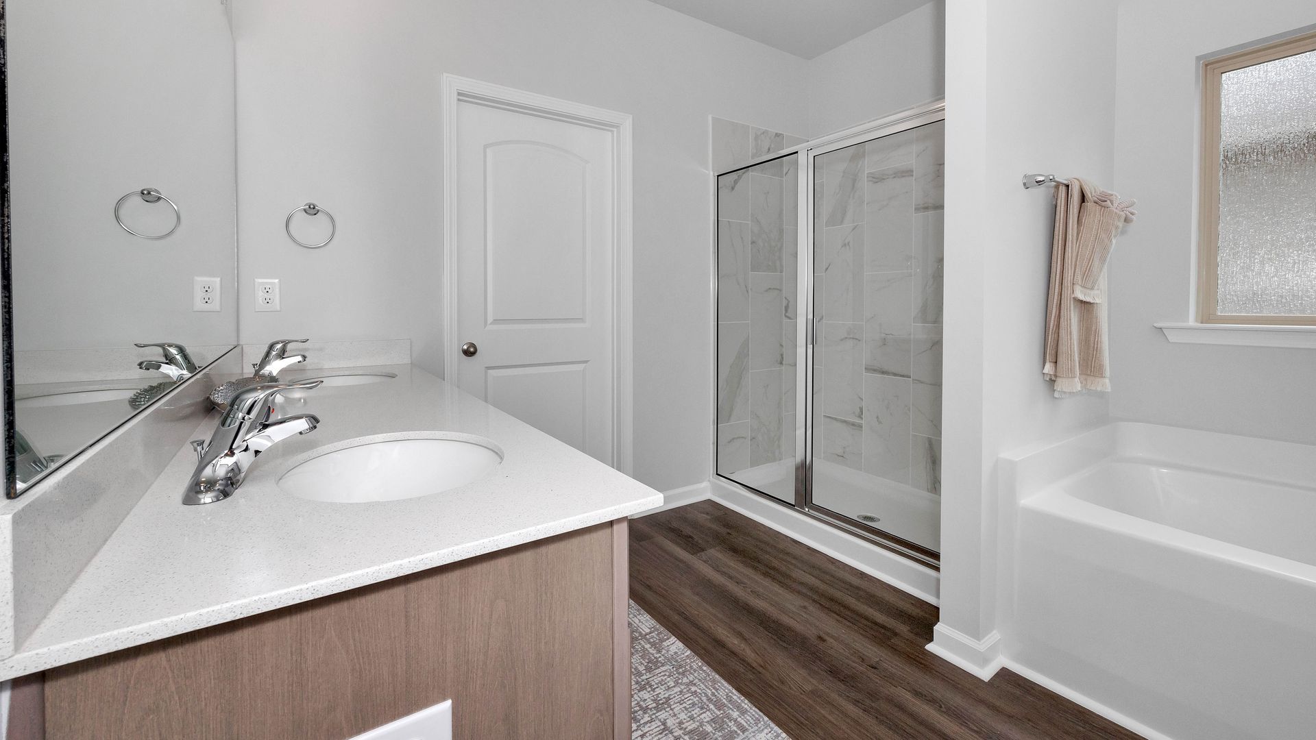 Bathroom with white walls, wood-look floor, vanity with oval sink, shower, and tub.