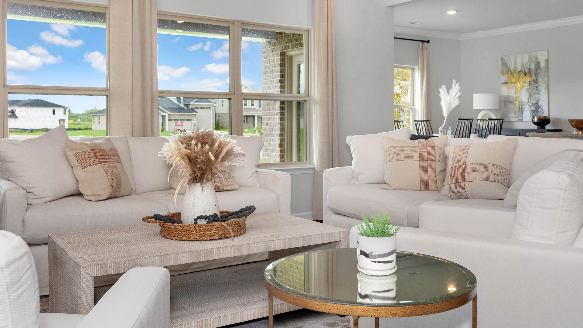 Living room with white sofas, beige pillows, wicker coffee table, and a round gold side table.