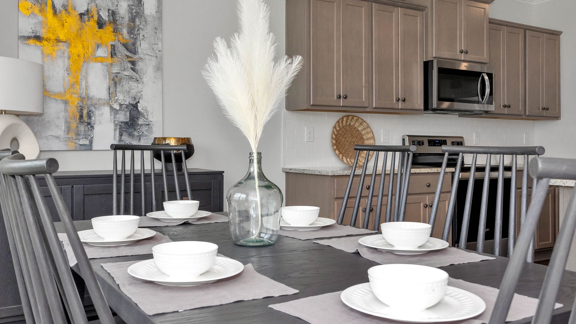 Dining room with a dark table set for six, grey chairs, and a kitchen in the background.