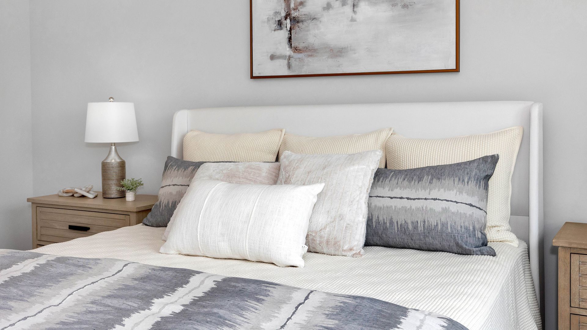 Cozy bedroom with white bed, pillows, and gray blanket, light wood nightstands, and art.